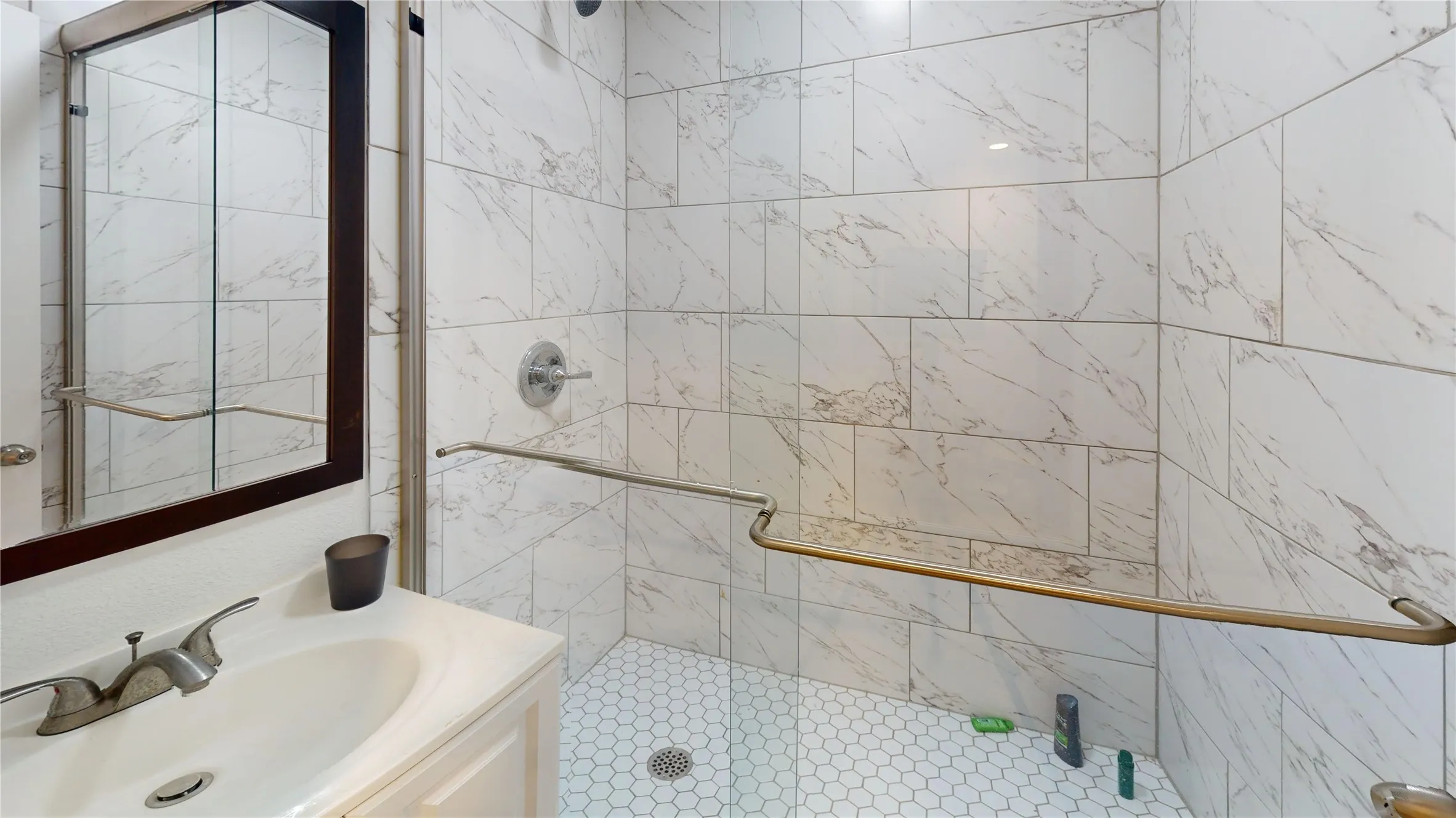 Shower featuring white rectangular marble-look wall tiles, hexagonal mosaic floor tiles, and a brushed nickel shower fixture