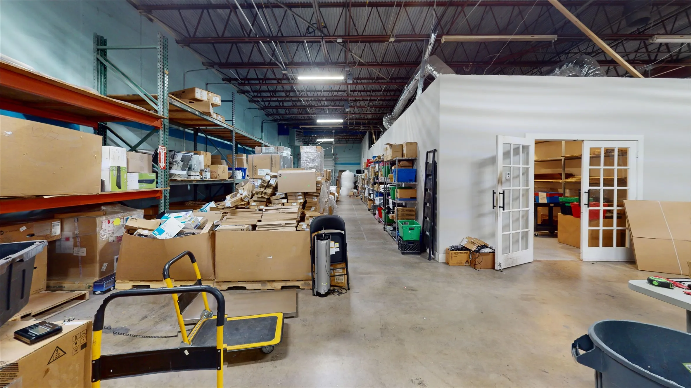 High-ceiling warehouse space featuring exposed overhead ductwork and concrete flooring