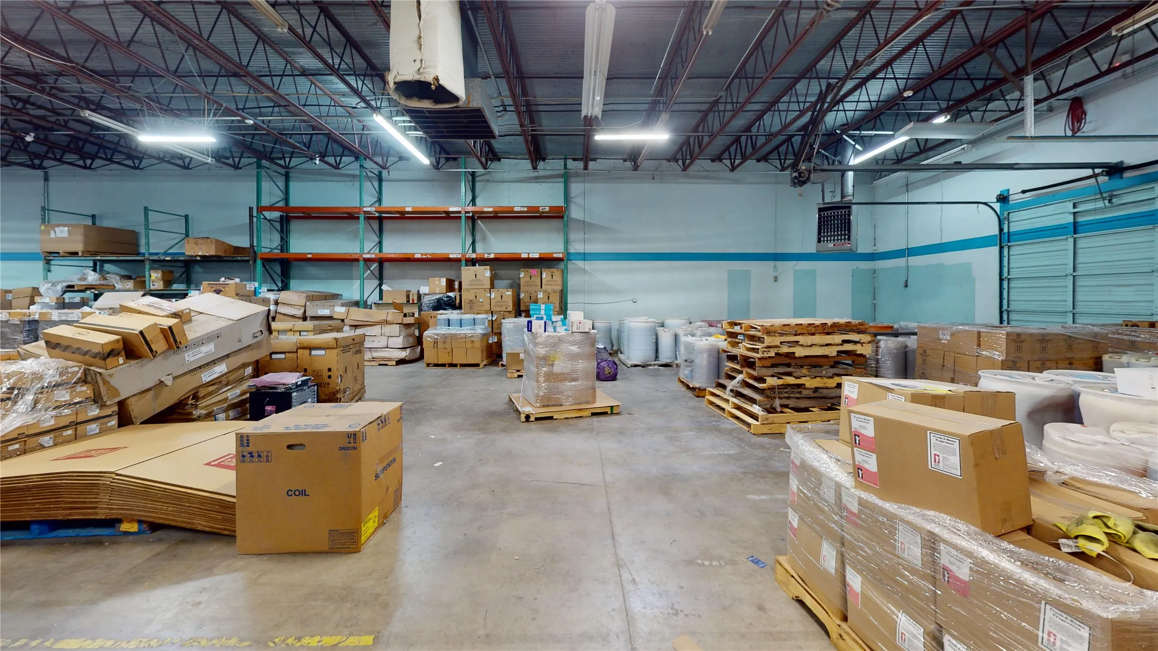 Spacious warehouse interior featuring high ceilings with exposed steel trusses, concrete flooring, and fluorescent lighting