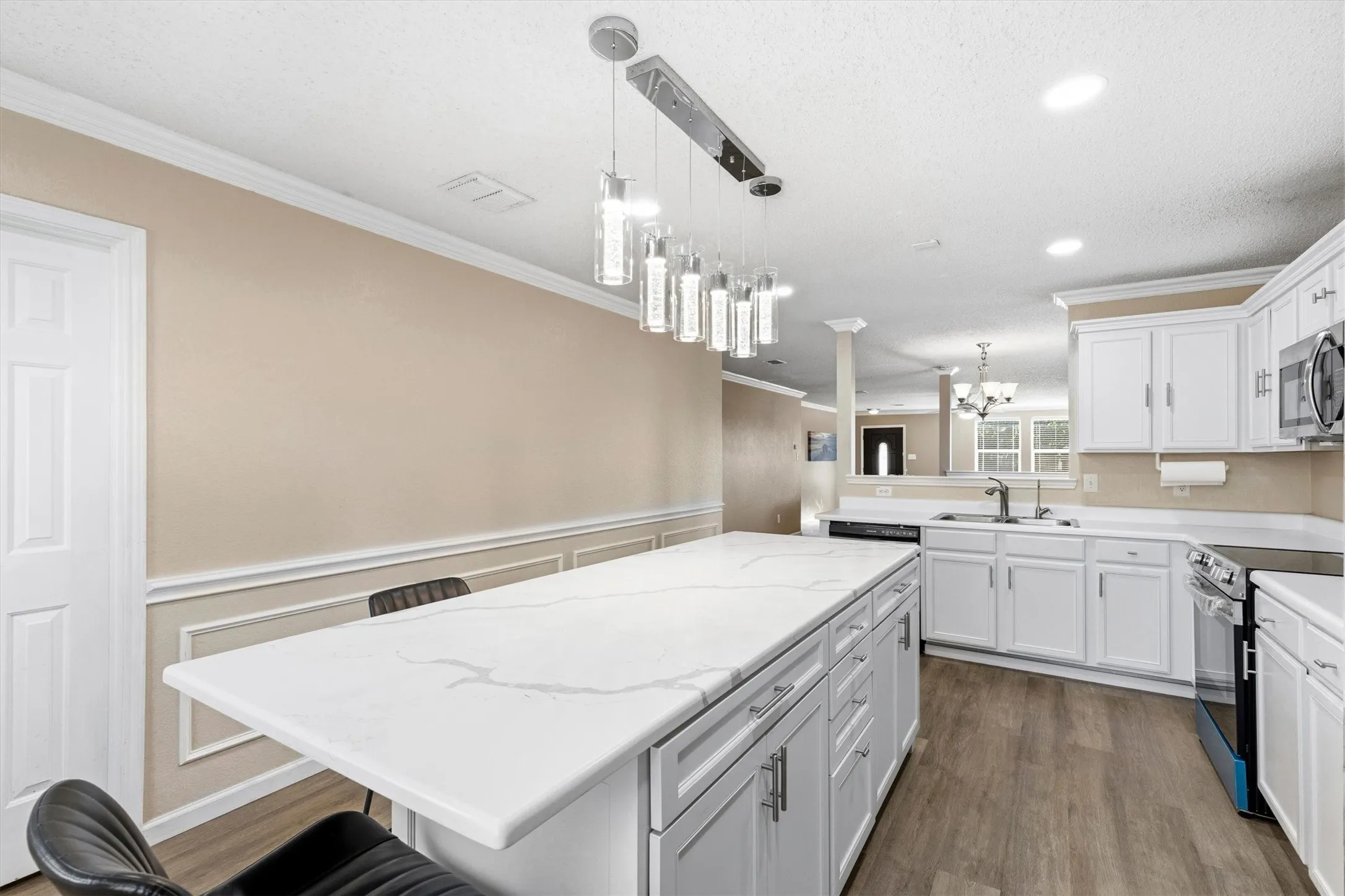Spacious kitchen featuring a large central island with a white surface, white cabinetry, integrated stainless steel appliances, and wood-finish flooring
