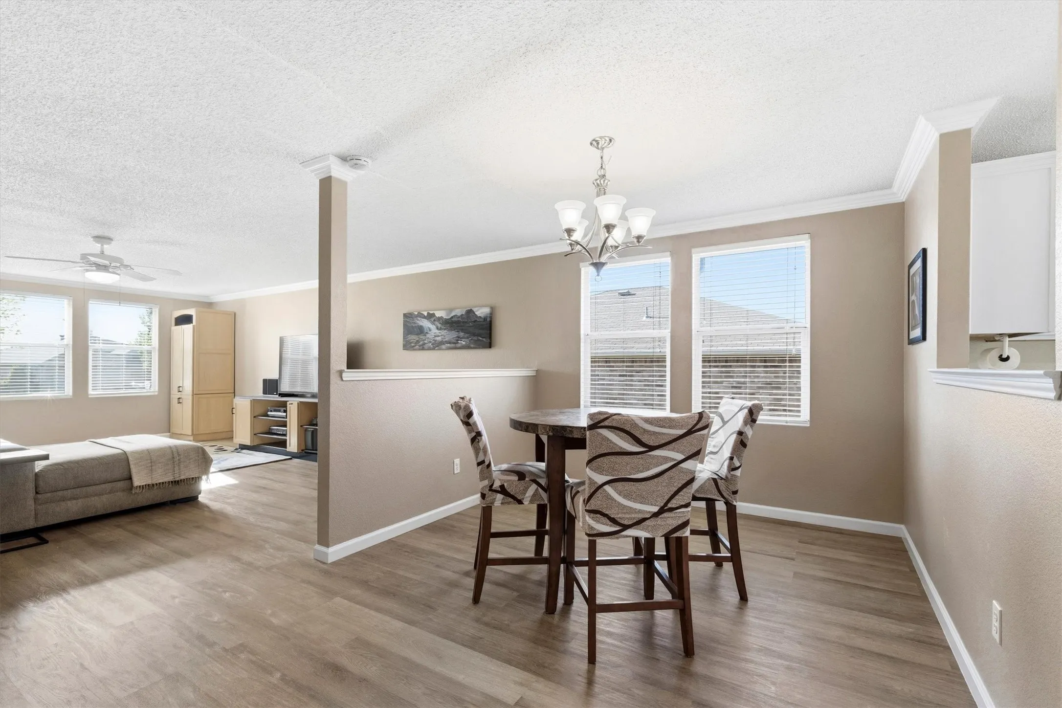 Open-concept living area featuring wood-finish flooring, crown molding, and multiple windows with blinds