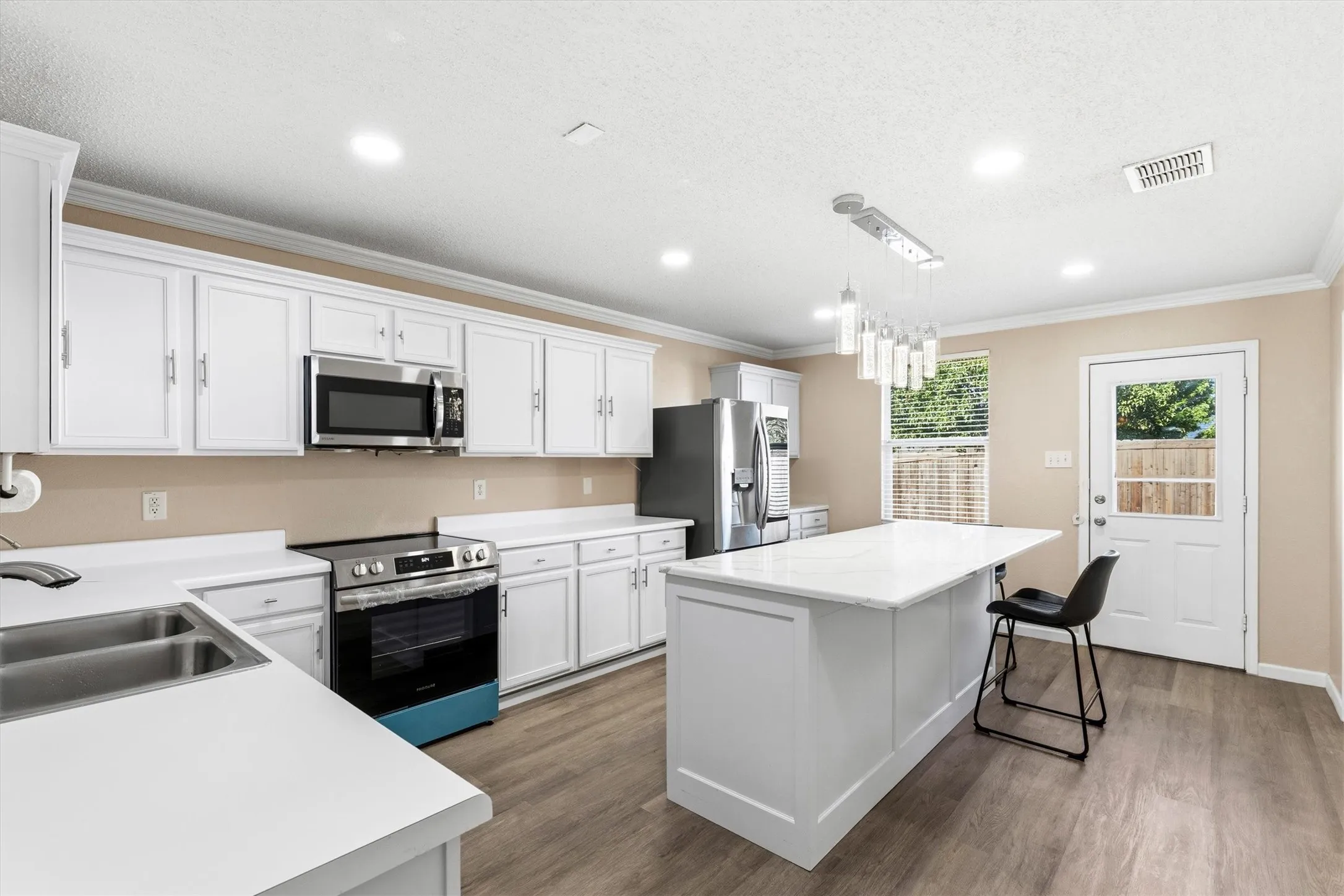 Kitchen featuring an expansive white quartz countertop island, stainless steel appliances, white cabinetry, wood-finish flooring, and recessed lighting