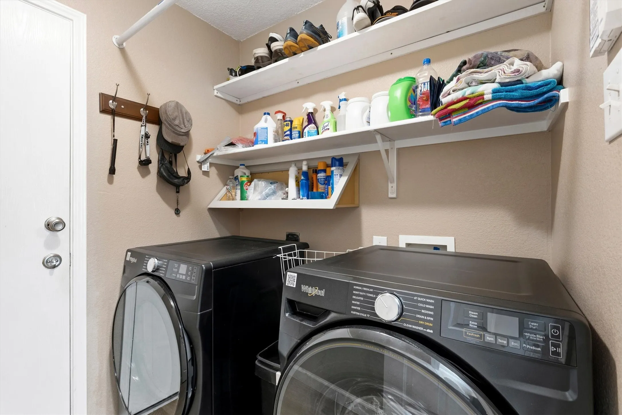 Dedicated laundry area featuring a front-load washer and dryer, multiple wall-mounted storage shelves, and a coat rack