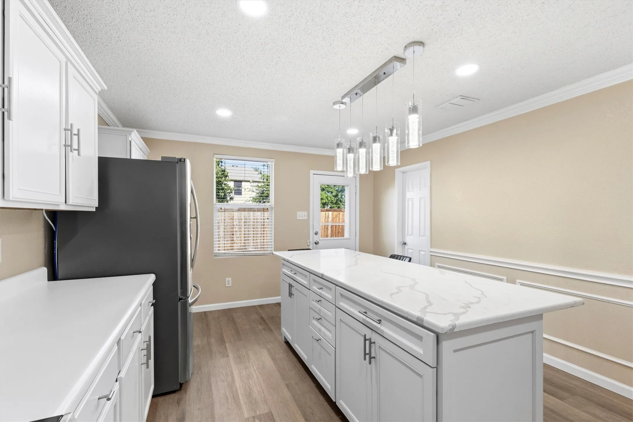 Modern kitchen island with a white veined countertop, pendant lighting, and ample cabinetry
