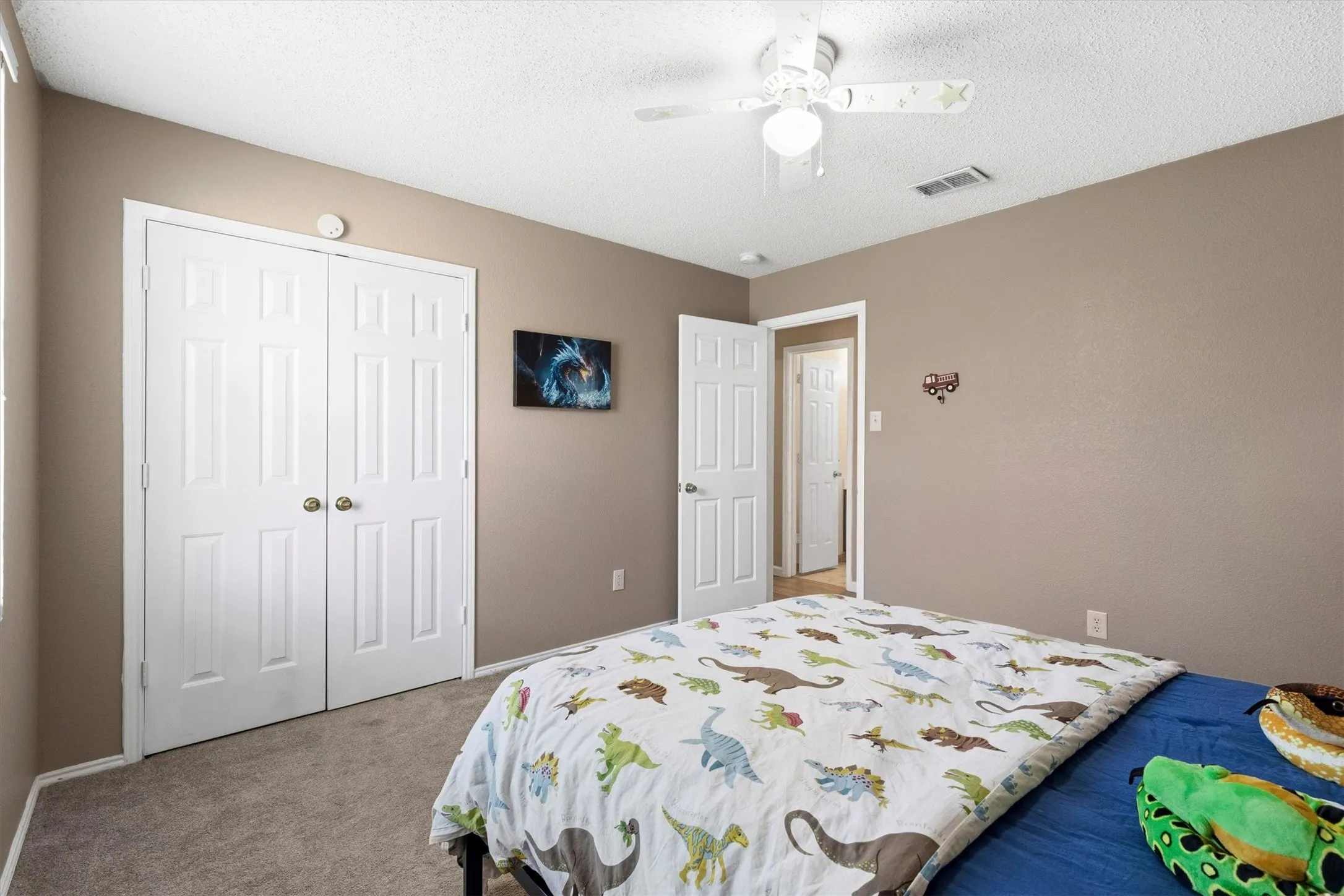 Interior room featuring neutral wall paint, gray carpeting, a ceiling fan with integrated lighting, and white bi-fold closet doors