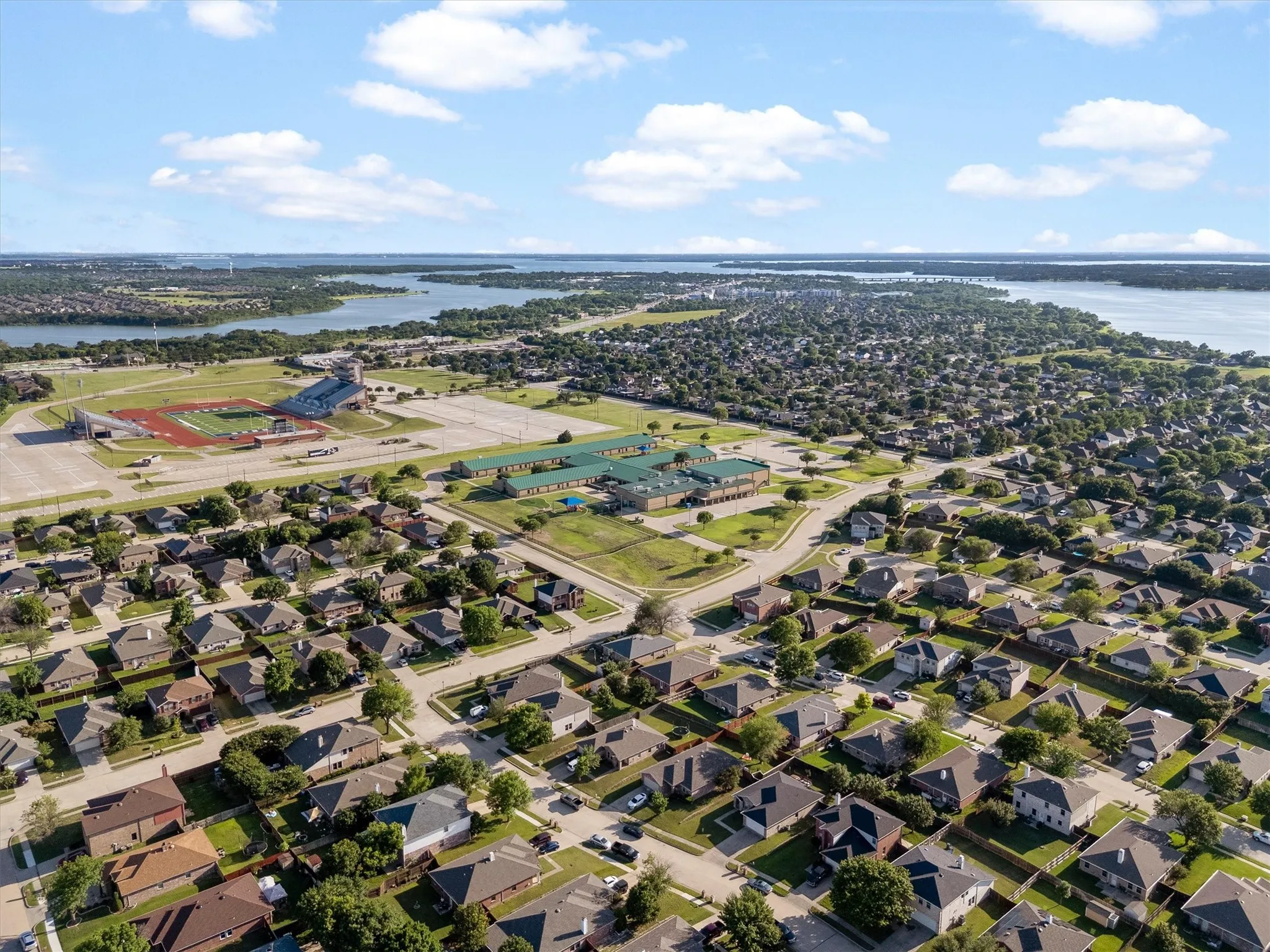 Aerial perspective showcasing a residential neighborhood with a stadium, school, and bodies of water