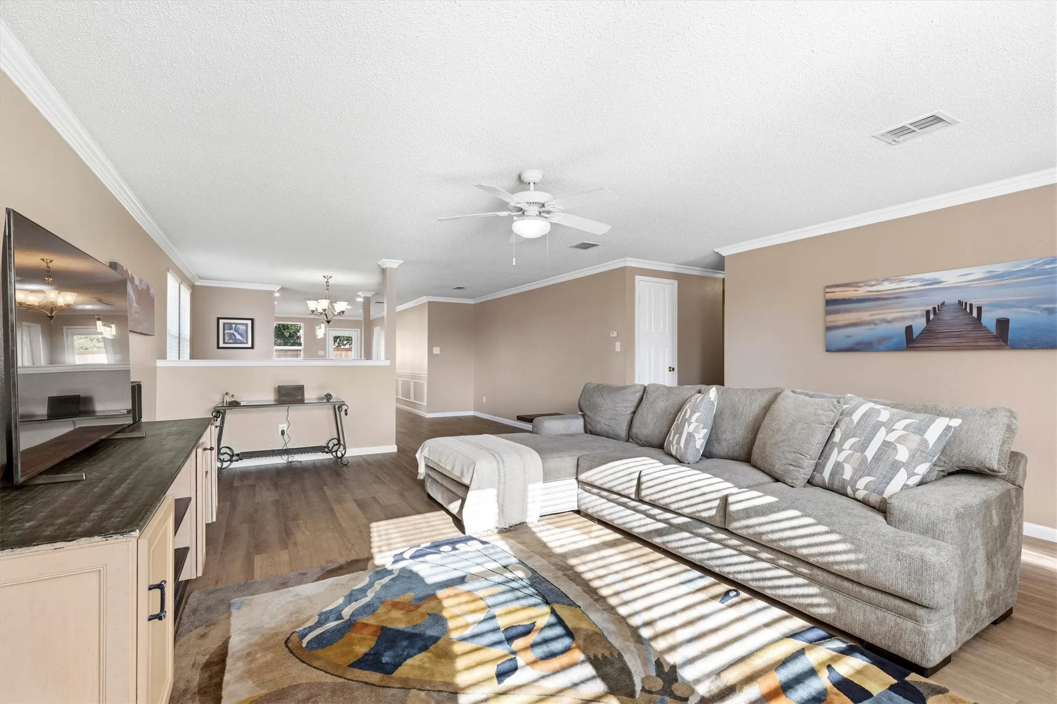 Open-concept living area with wood-finish flooring, crown molding, and recessed lighting