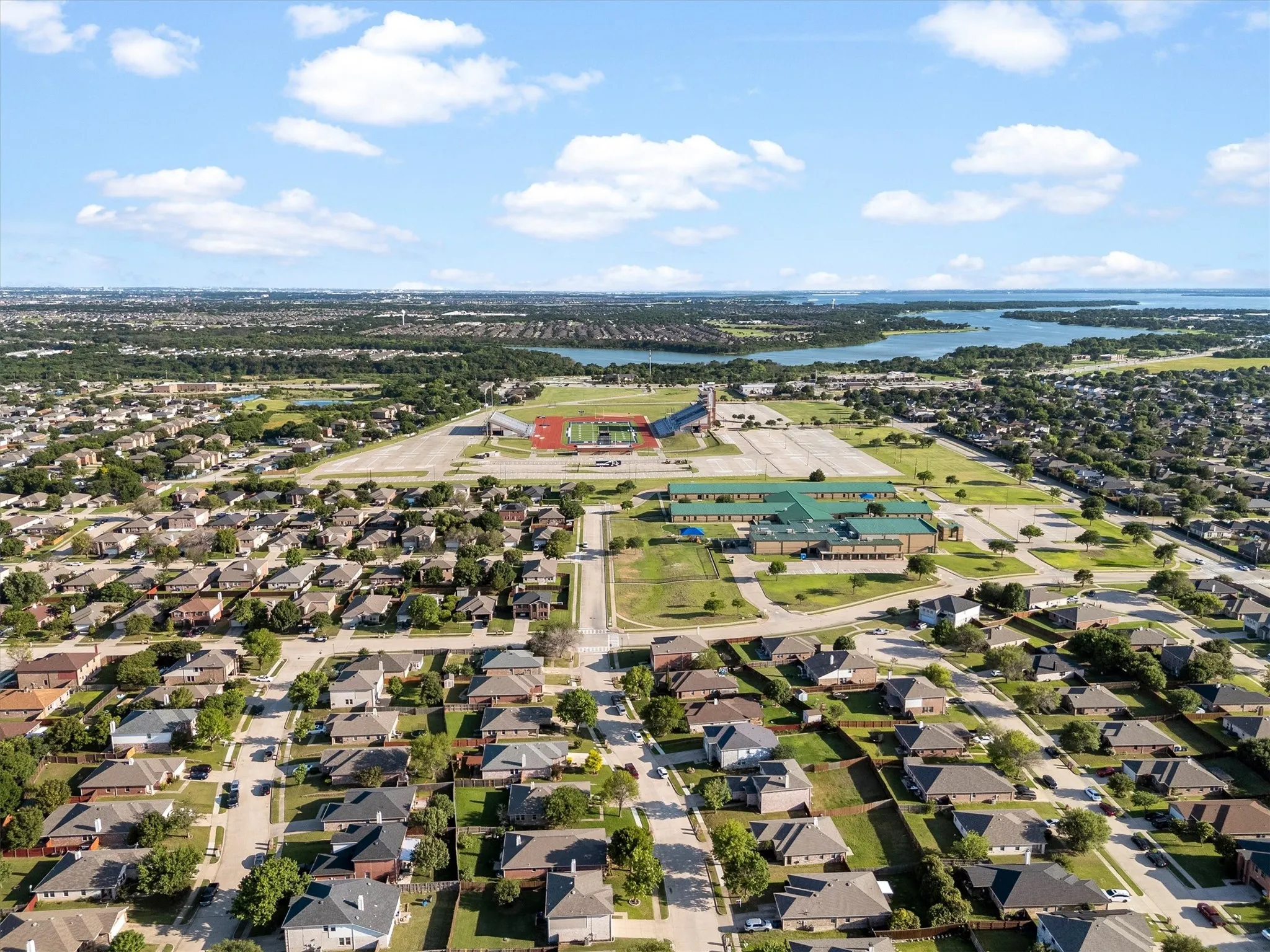 Expansive residential area featuring numerous single-story homes, a large athletic complex with tracks and fields, and a prominent academic facility with a green roof