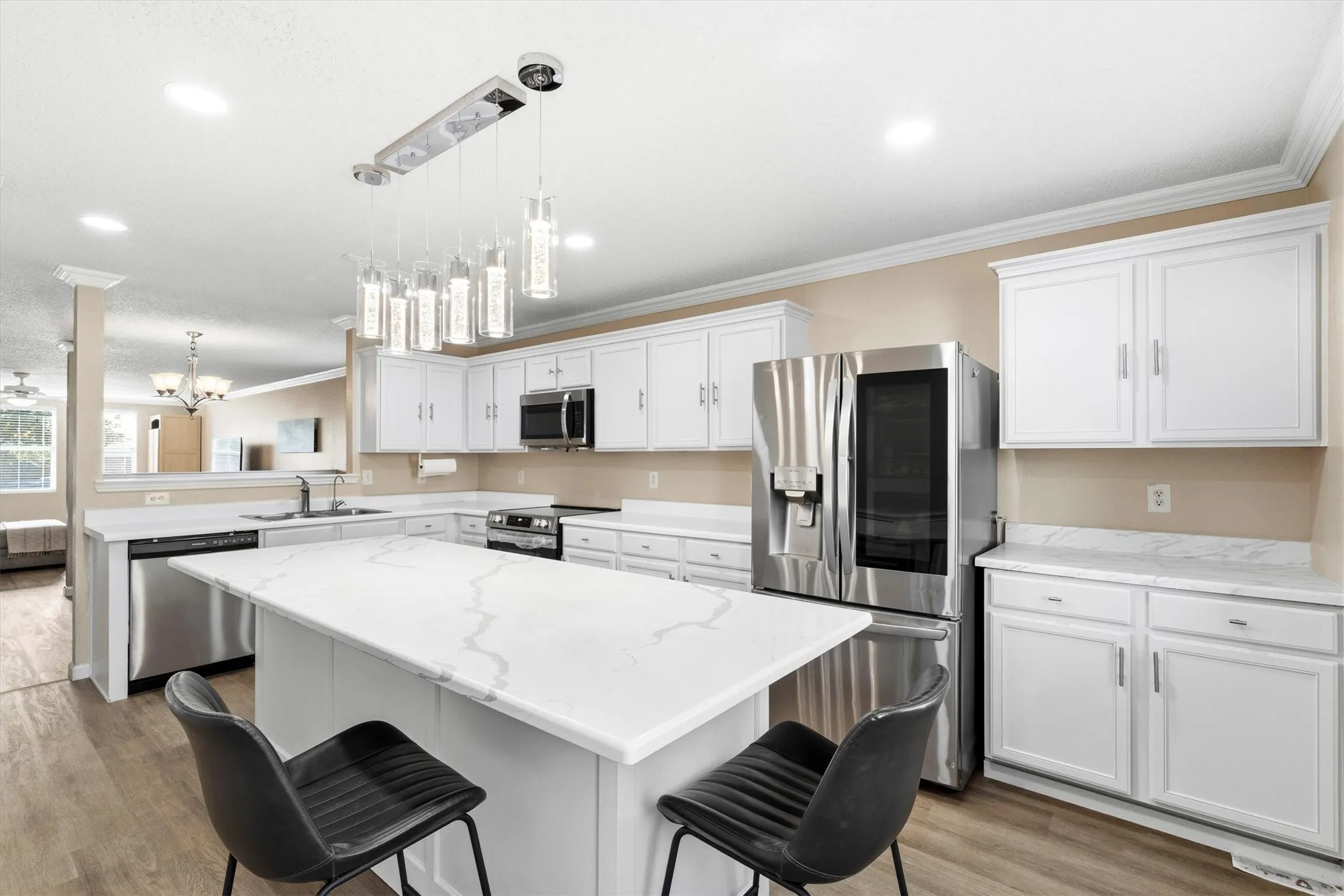 Open-concept kitchen featuring a central island with a stone-finish countertop, white cabinetry, stainless steel appliances, and wood-finish flooring