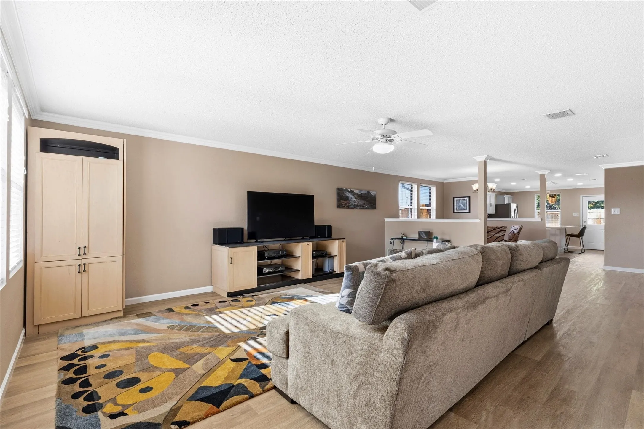 Spacious living area featuring light wood-finish flooring, a ceiling fan, and crown molding