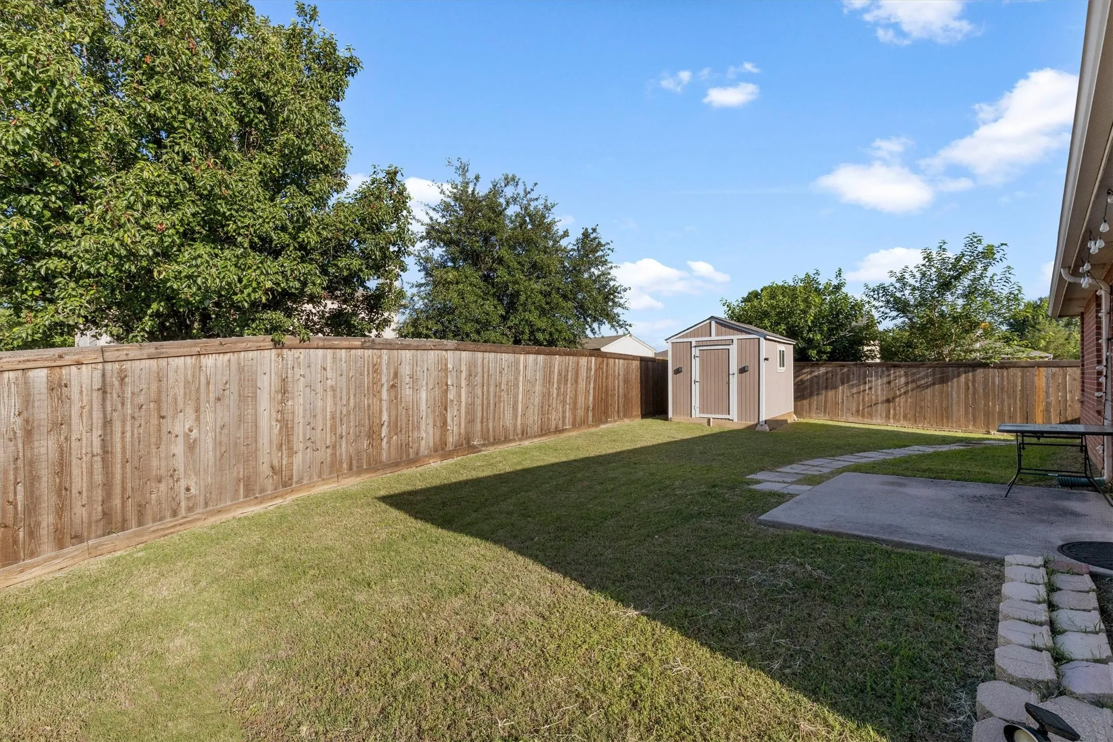 Spacious backyard featuring a manicured lawn, a privacy fence, a storage shed, a concrete patio, and stone pavers