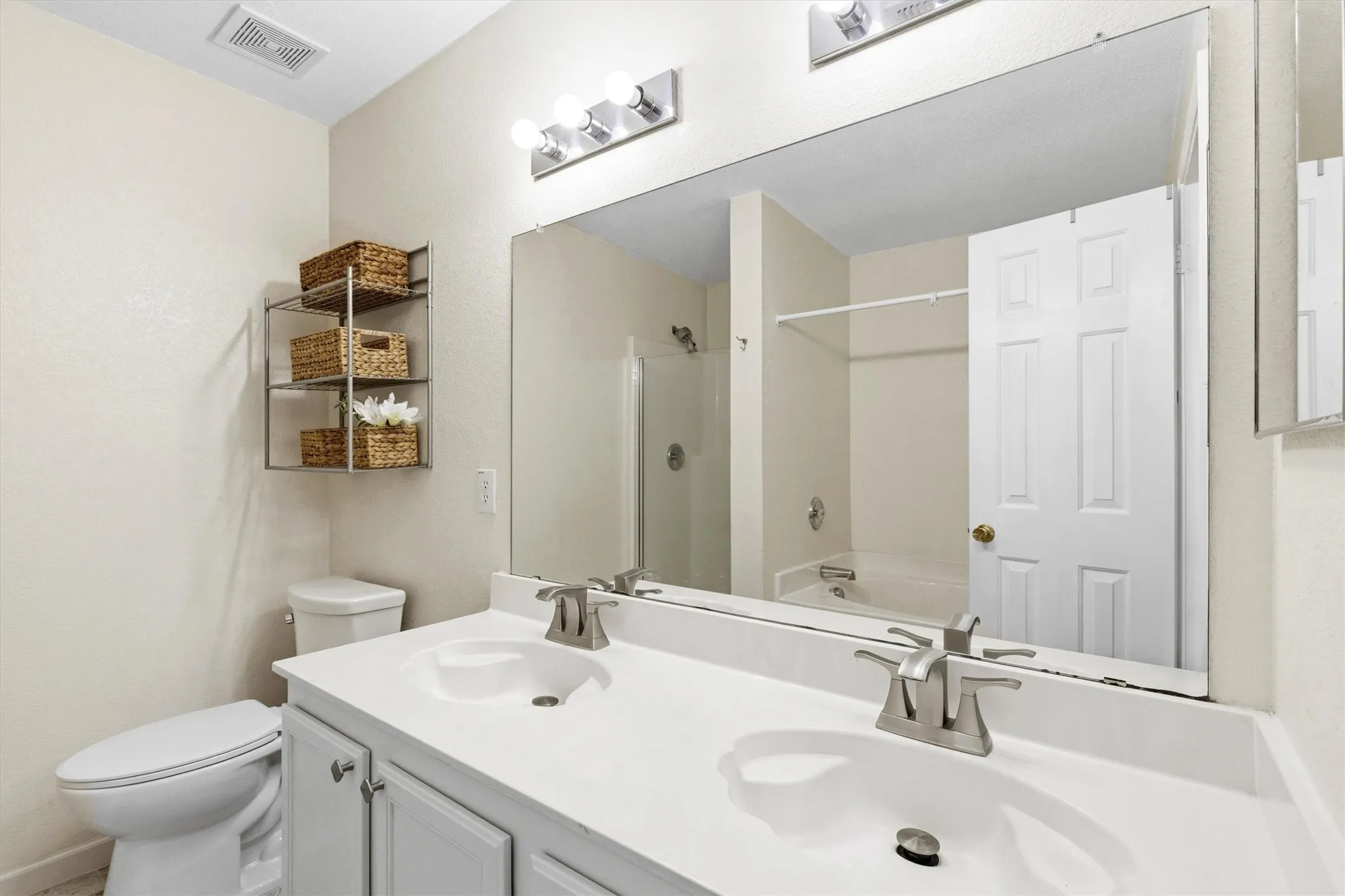 Bathroom featuring a dual sink vanity with white countertops and cabinetry, brushed nickel faucets, a large wall-mounted mirror, and a built-in shower/tub combination