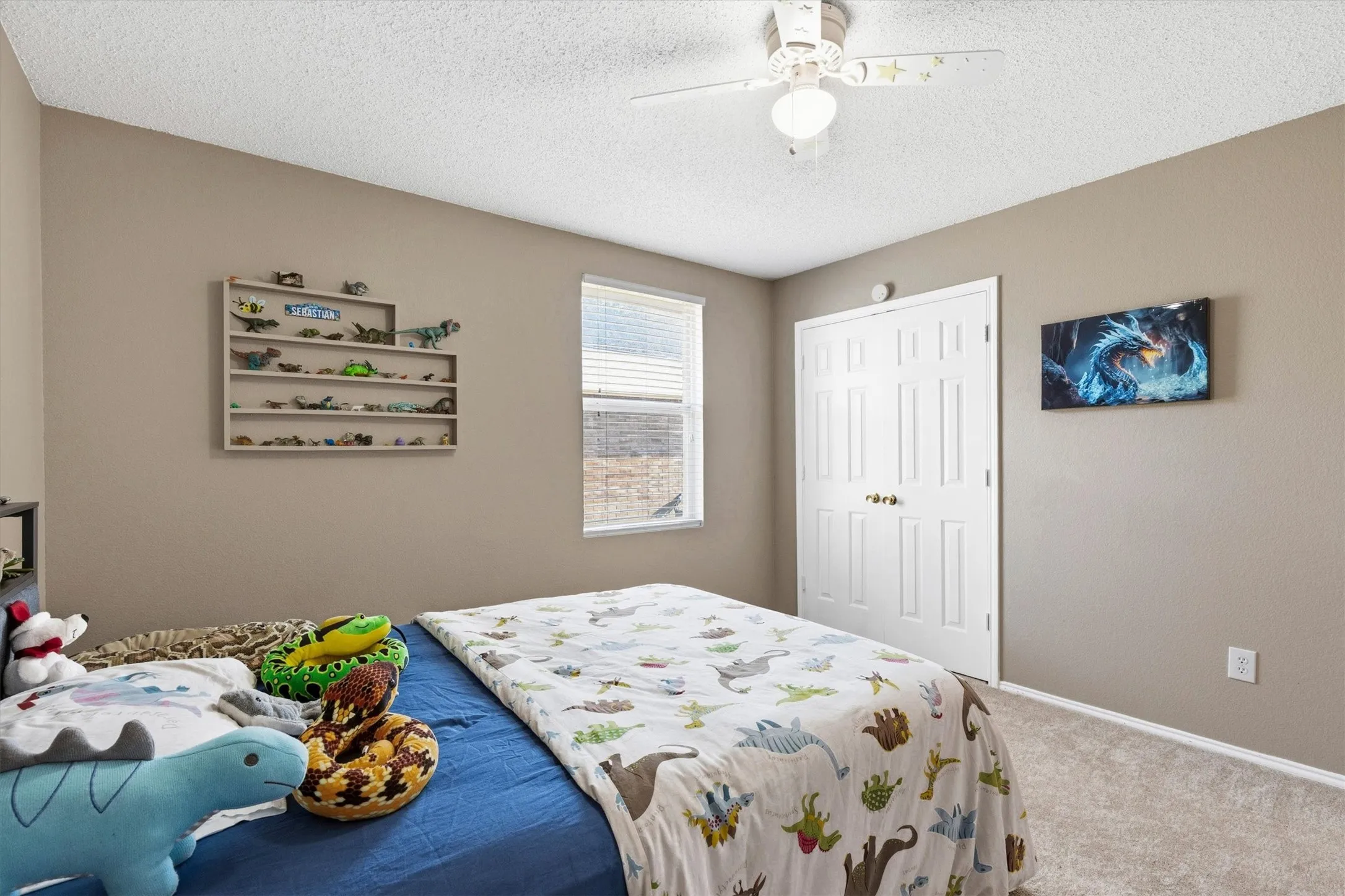 Neutral-toned bedroom featuring a textured carpet floor, a white ceiling fan with integrated lighting, and a window with horizontal blinds