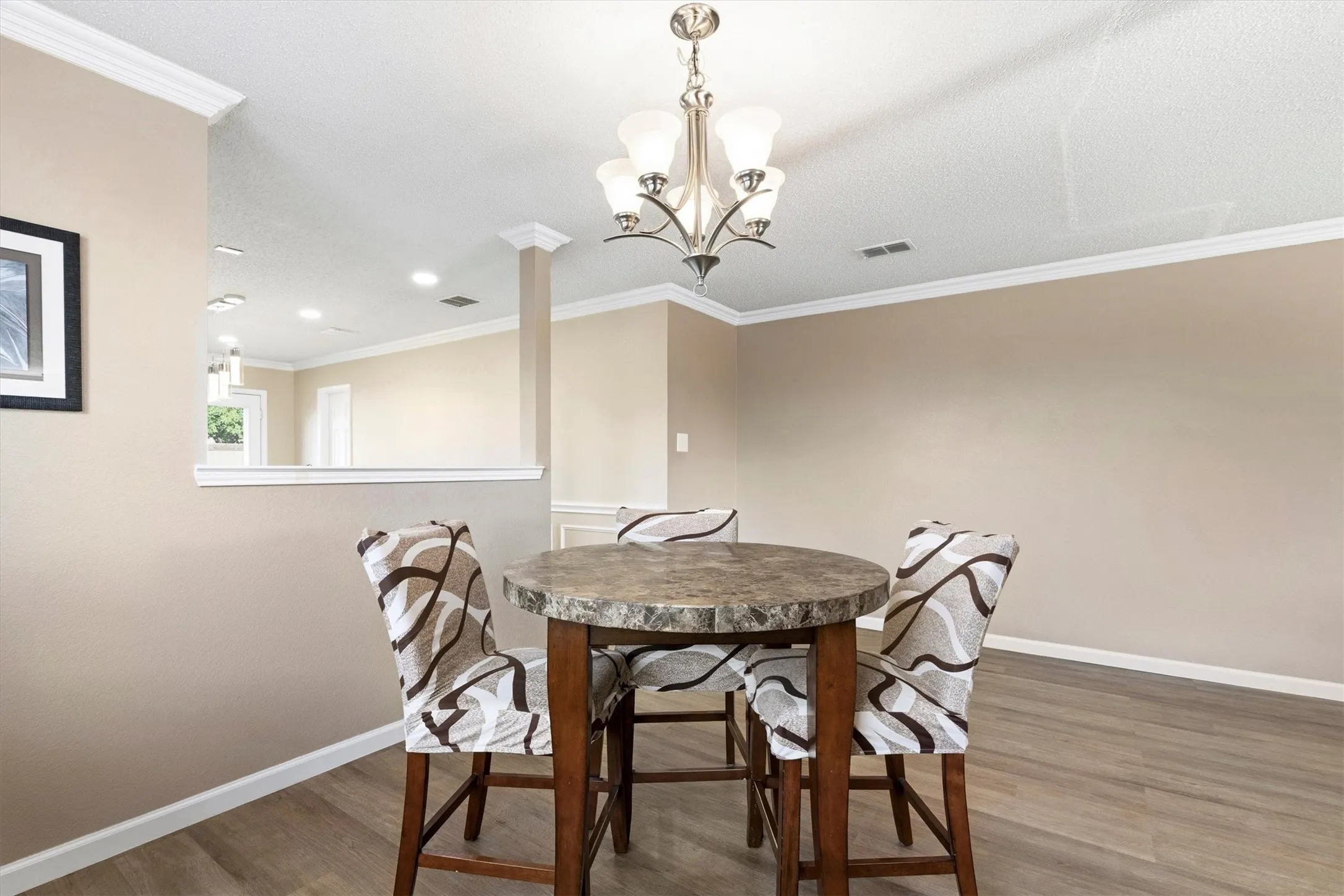 Dining area featuring wood-finish flooring, a decorative chandelier, crown molding, a half-wall, and neutral wall tones