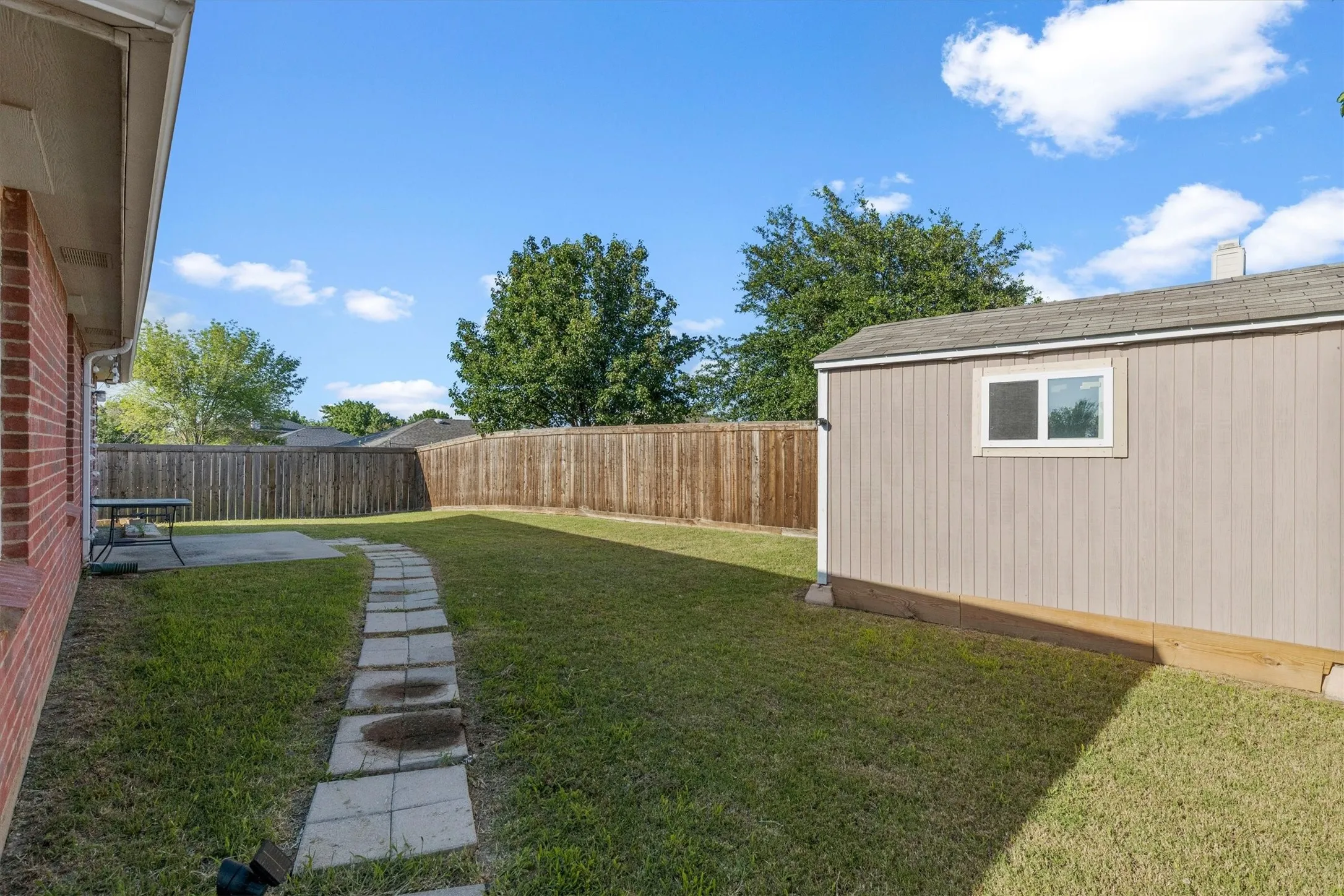 Expansive backyard featuring a manicured lawn, a stone paver pathway, and a privacy fence