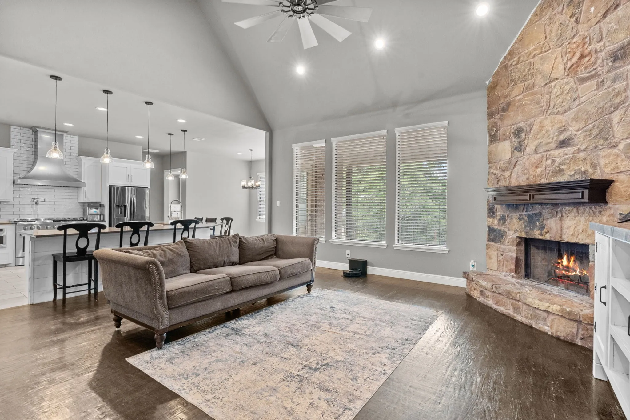 Living room featuring dark hardwood / wood-style floors, ceiling fan with notable chandelier, a stone fireplace, and high vaulted ceiling