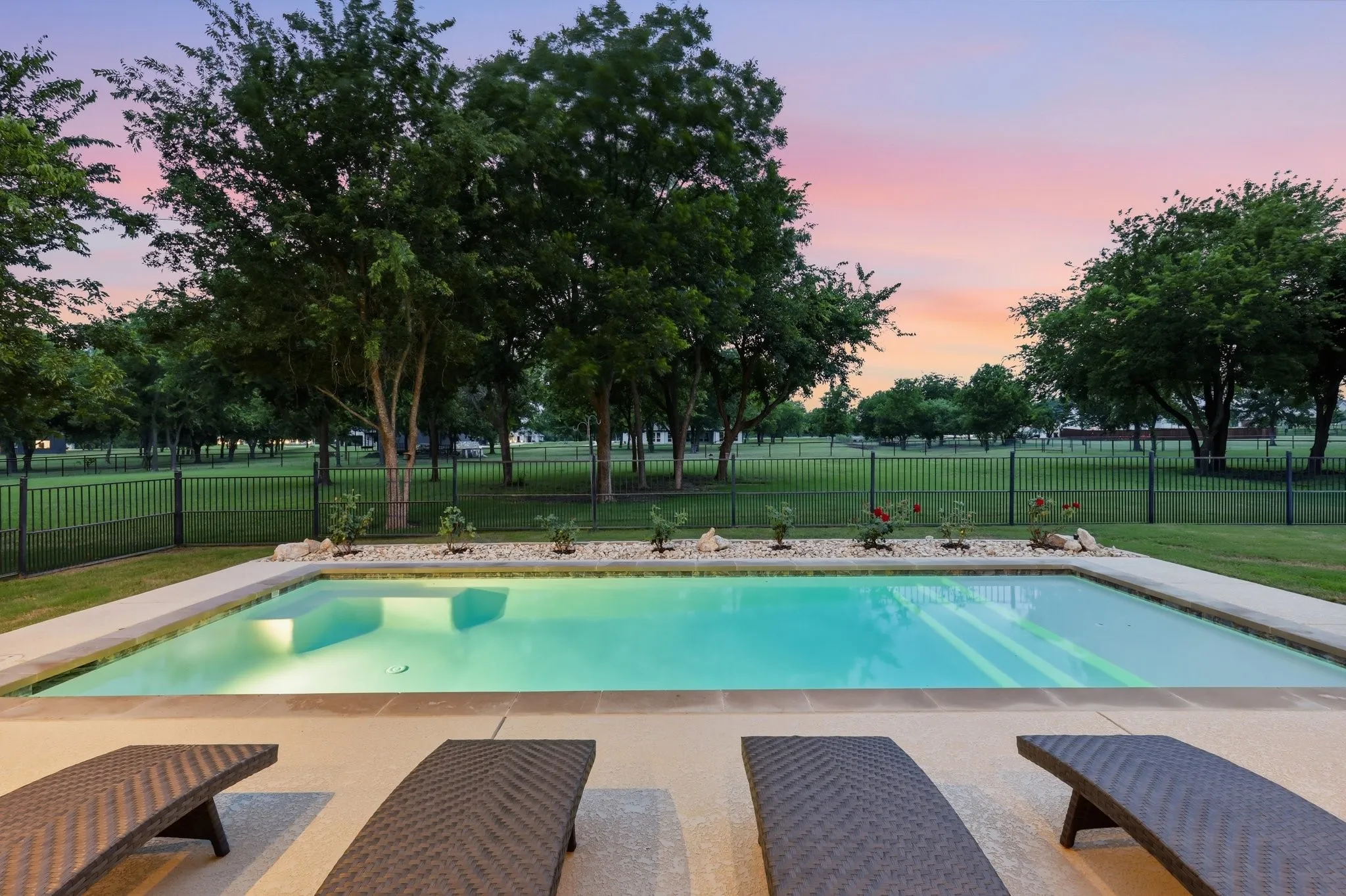 Rectangular in-ground pool with integrated steps, surrounded by a concrete deck and a bed of white stones with plantings