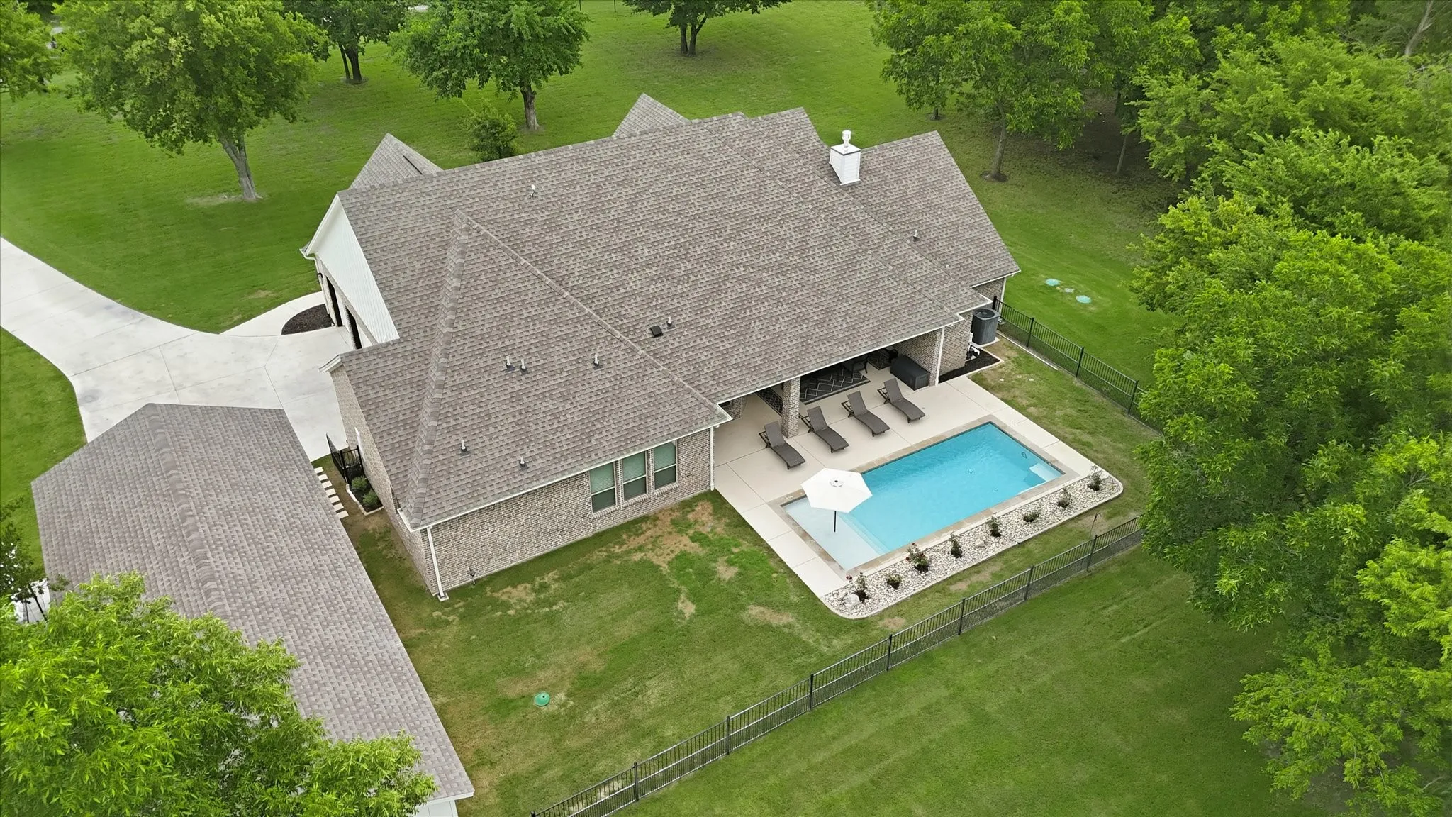Expansive backyard featuring a rectangular pool with integrated steps, surrounded by a concrete patio and a black metal fence