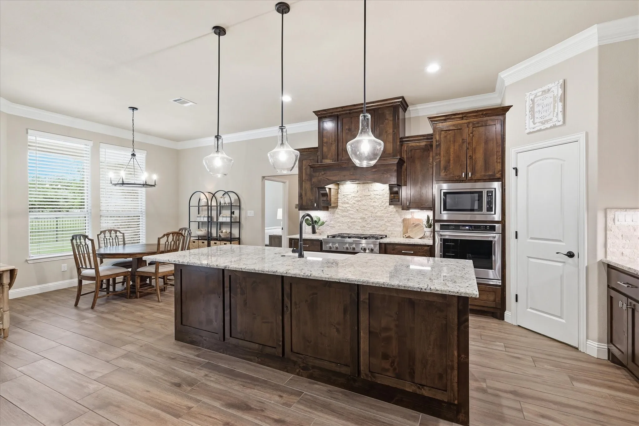 Kitchen featuring a large island with a light-toned countertop, dark wood-finish cabinetry, stainless steel appliances, a stone backsplash, and wood-finish flooring