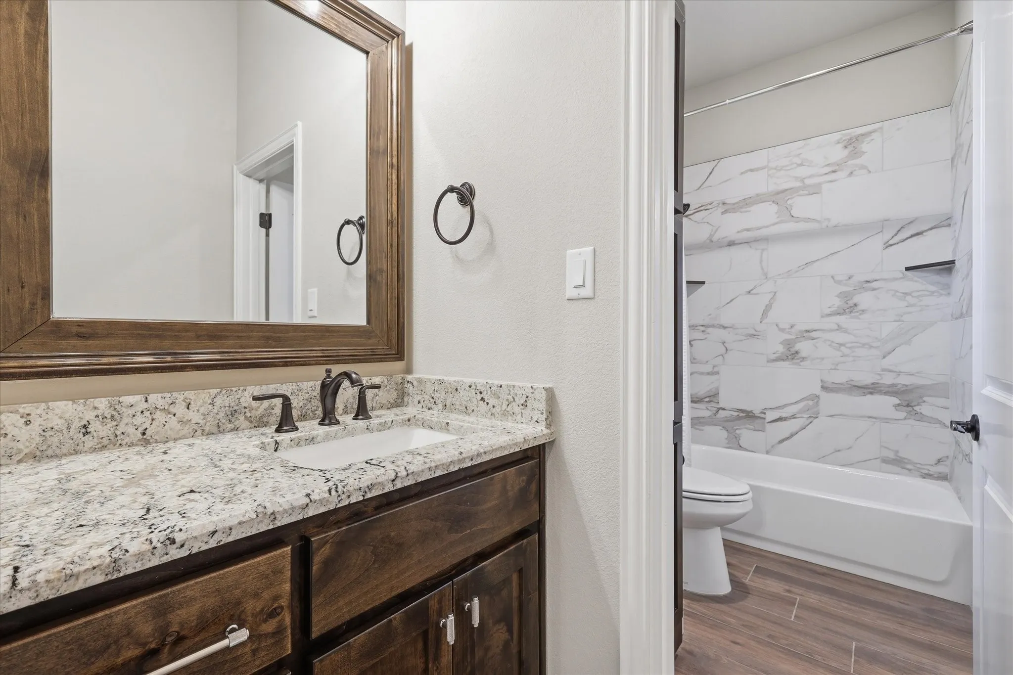 Bathroom featuring a wood-framed mirror, double vanity with stone countertop, and wood-finish cabinetry