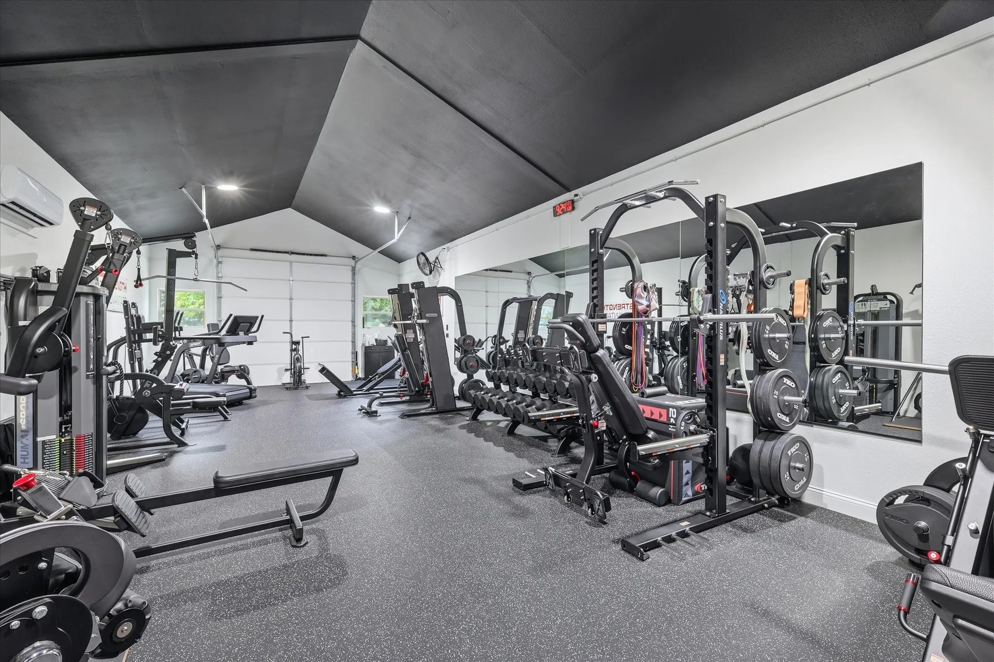 Dedicated fitness space featuring rubber flooring, high vaulted ceilings, integrated lighting, and a full-wall mirror