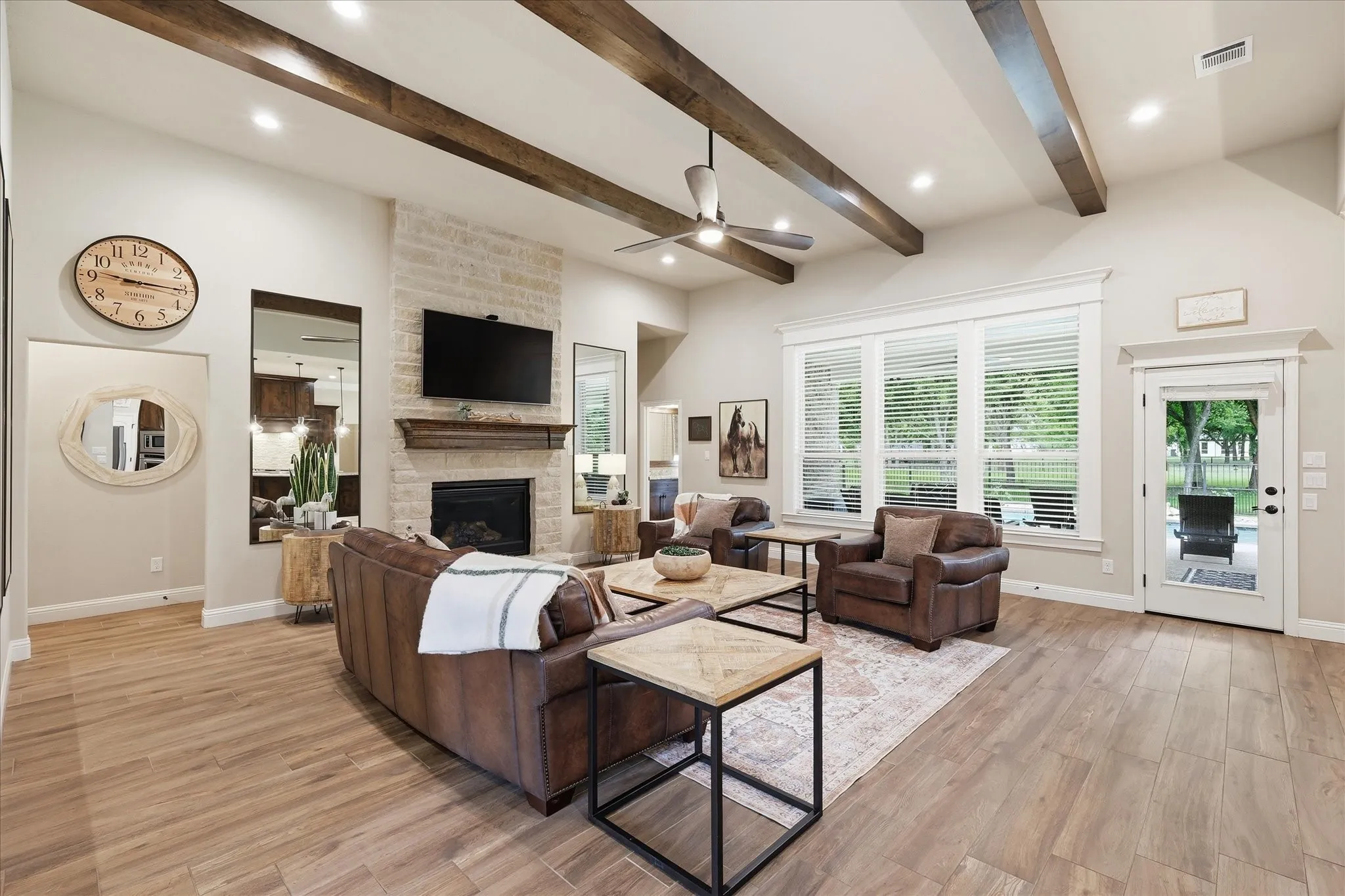 Spacious living area featuring a stone-clad fireplace, wood-finish flooring, vaulted ceiling with exposed beams, and ample natural light from large windows