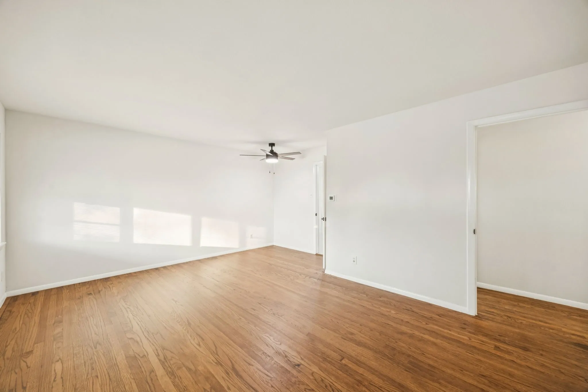 Spacious interior featuring wood-finish flooring, white walls, and a ceiling fan