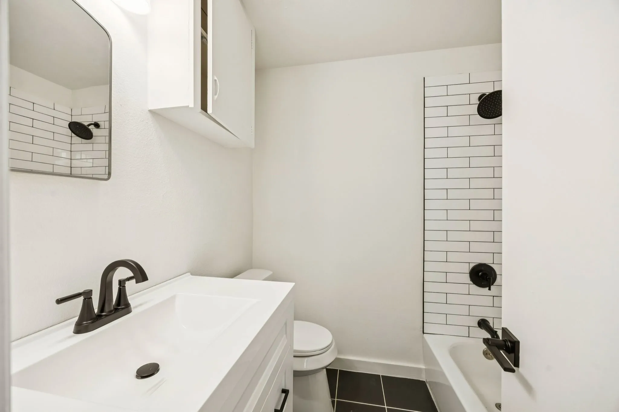 Bathroom featuring a white vanity with integrated sink, dark bronze-finish fixtures, and a subway tile shower surround, freshly remodeled