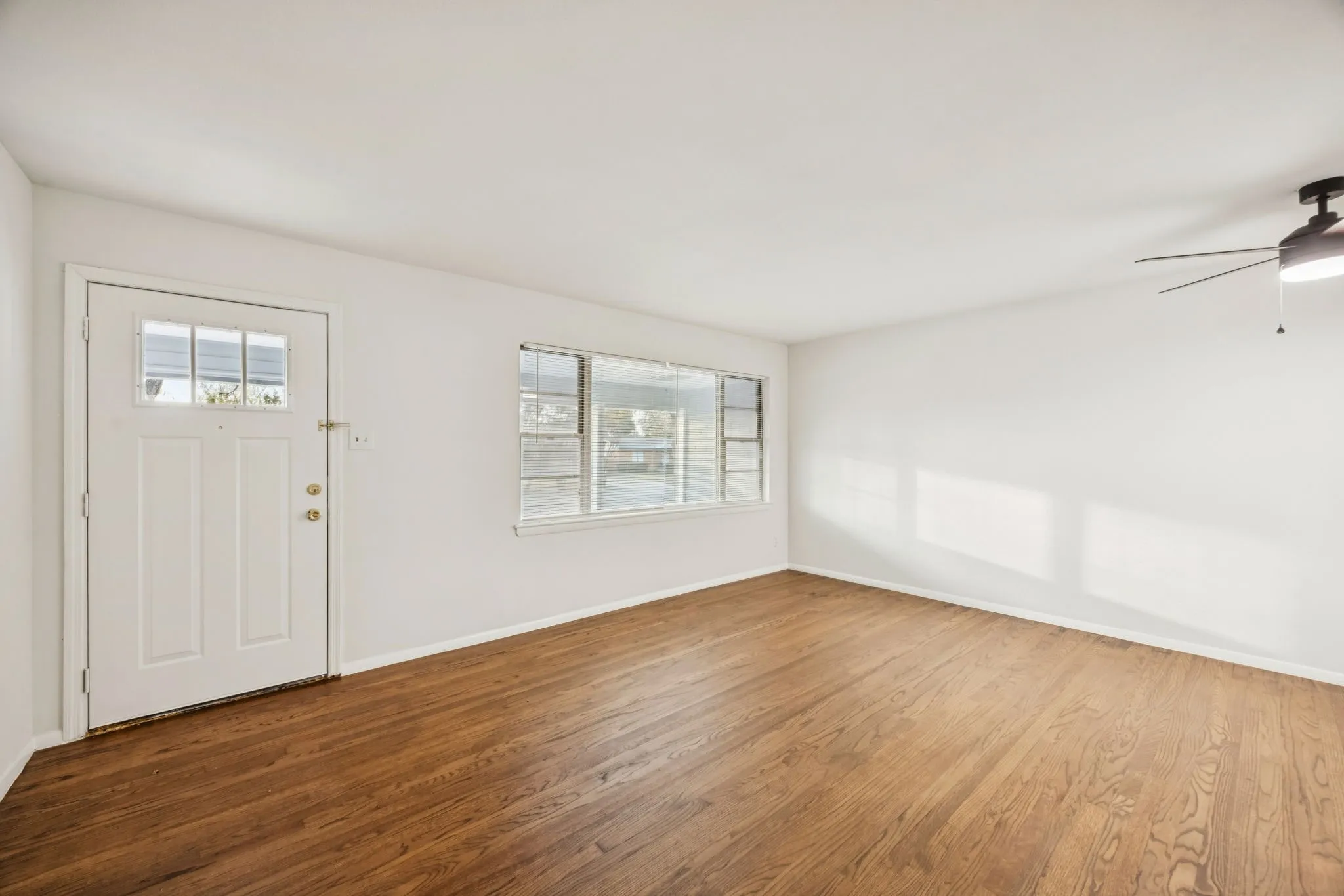 Spacious room featuring wood-finish flooring, a multi-pane front door, and a horizontal window with multiple panes