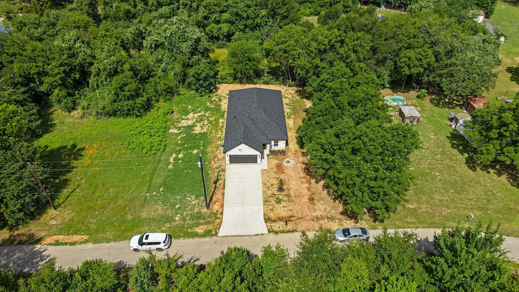 Newly constructed single-story residence featuring an attached garage and a long concrete driveway, surrounded by mature trees and natural landscaping