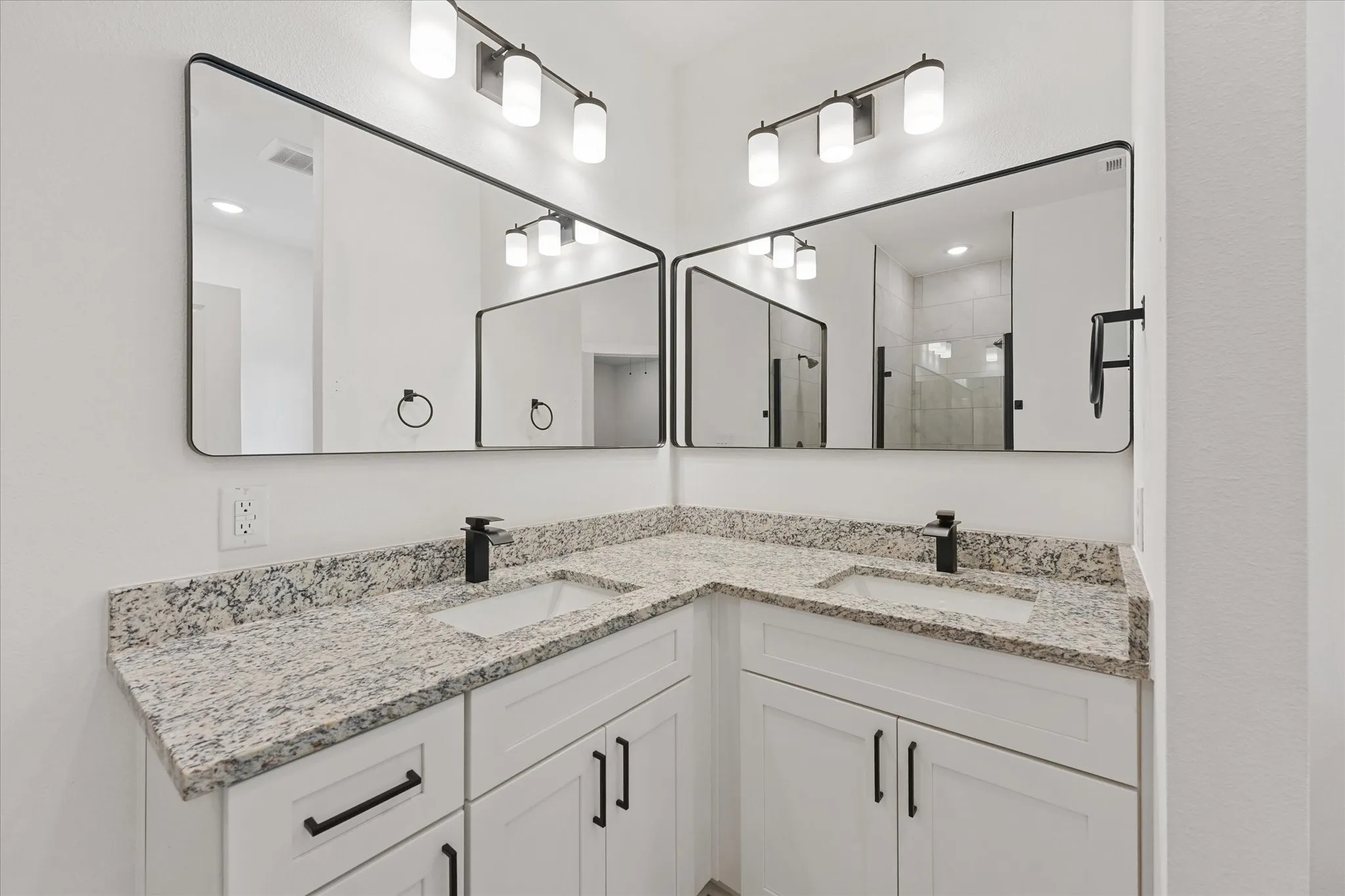 Dual vanity featuring white shaker cabinetry, speckled countertops, matte black hardware and fixtures, and rectangular framed mirrors