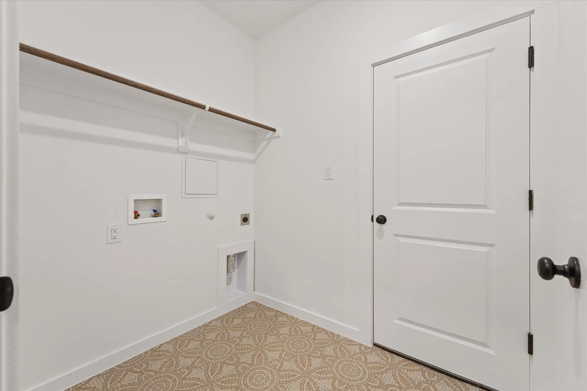 Dedicated utility area featuring patterned flooring, a white paneled door with matte black hardware, and an overhead shelving unit with a hanging rod