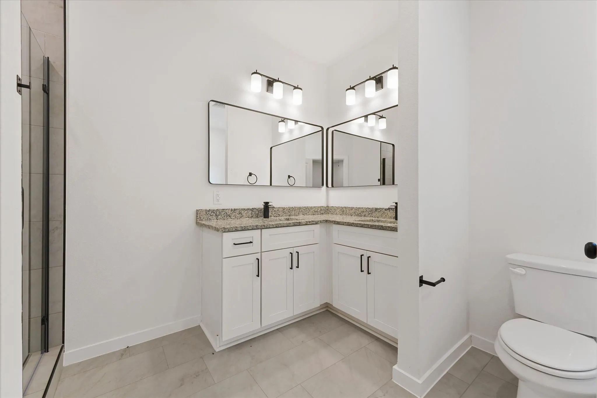 Modern bathroom featuring a dual vanity with granite countertops, white cabinetry, and matte black hardware