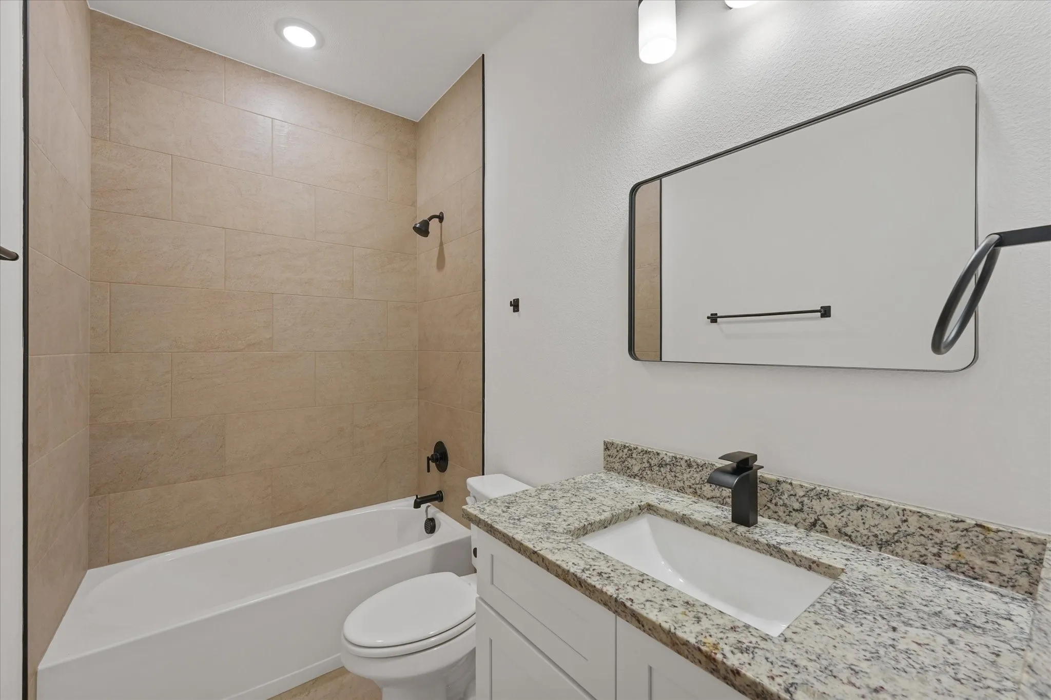 Bathroom featuring a tub/shower combination with tile surround, a single vanity with stone countertop, and a contemporary mirror