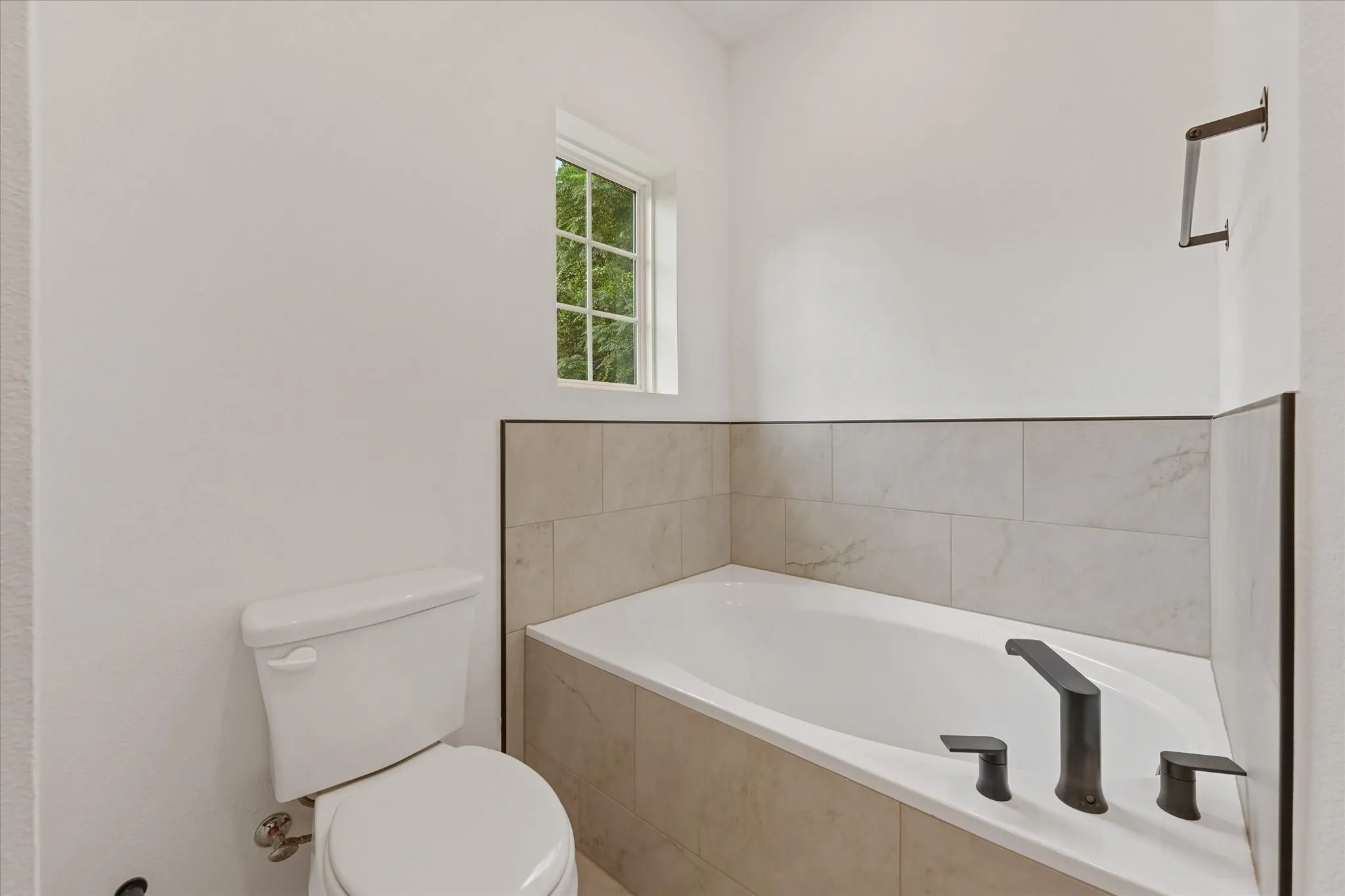 Corner soaking tub with dark bronze fixtures, complemented by light-toned wall tiling and a grid-patterned window