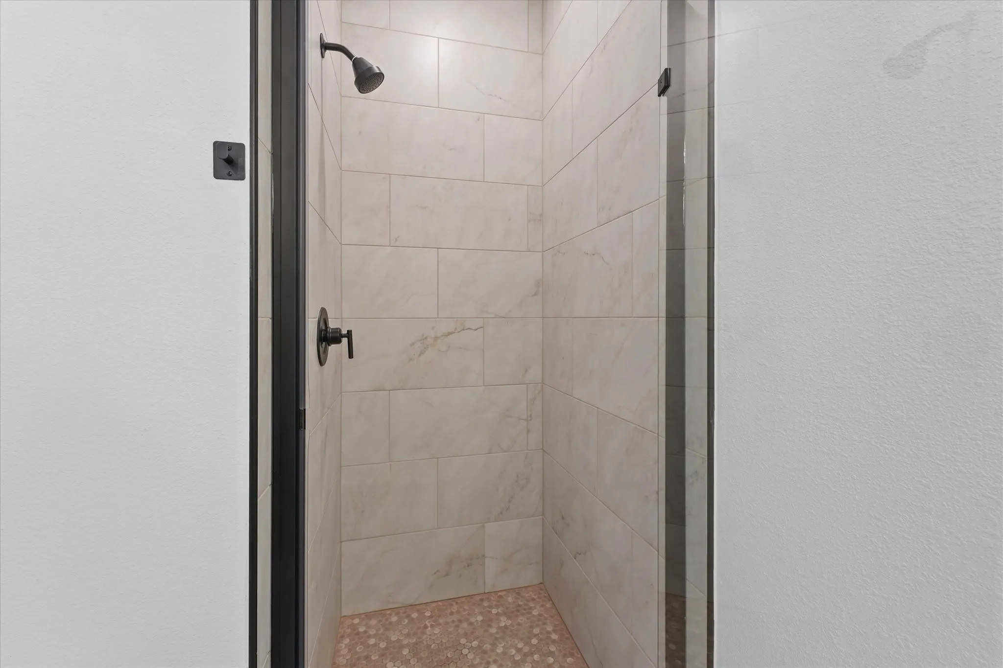Walk-in shower with light-toned tiled walls, matte black fixtures, and a pebble-tiled floor