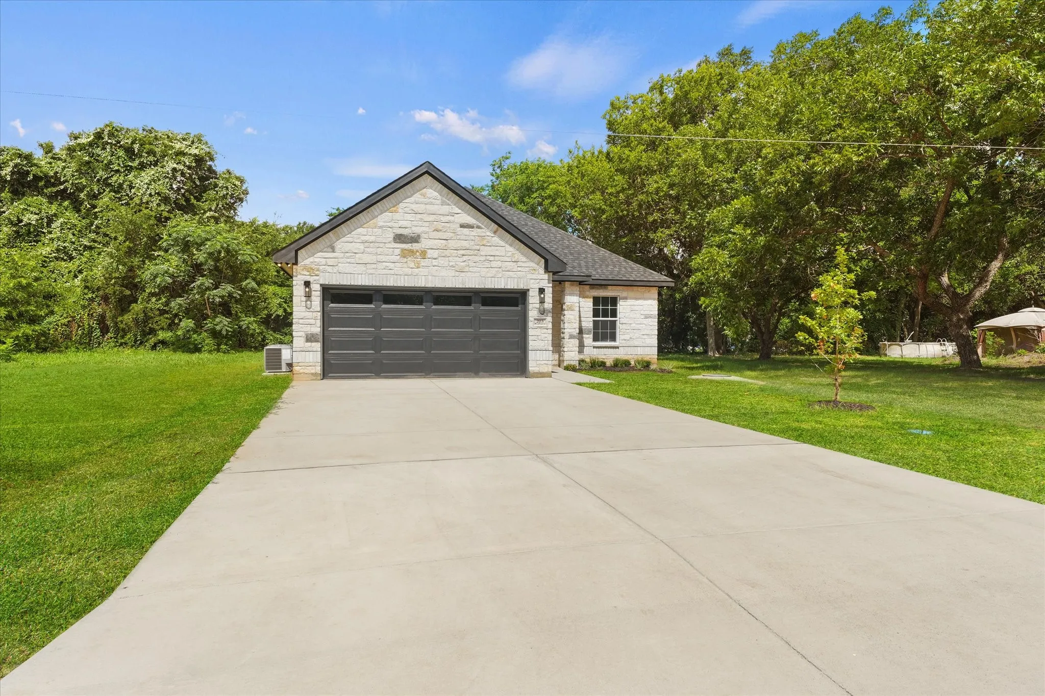 Stone facade residence with a dark gray sectional garage door, a concrete driveway, and a manicured lawn