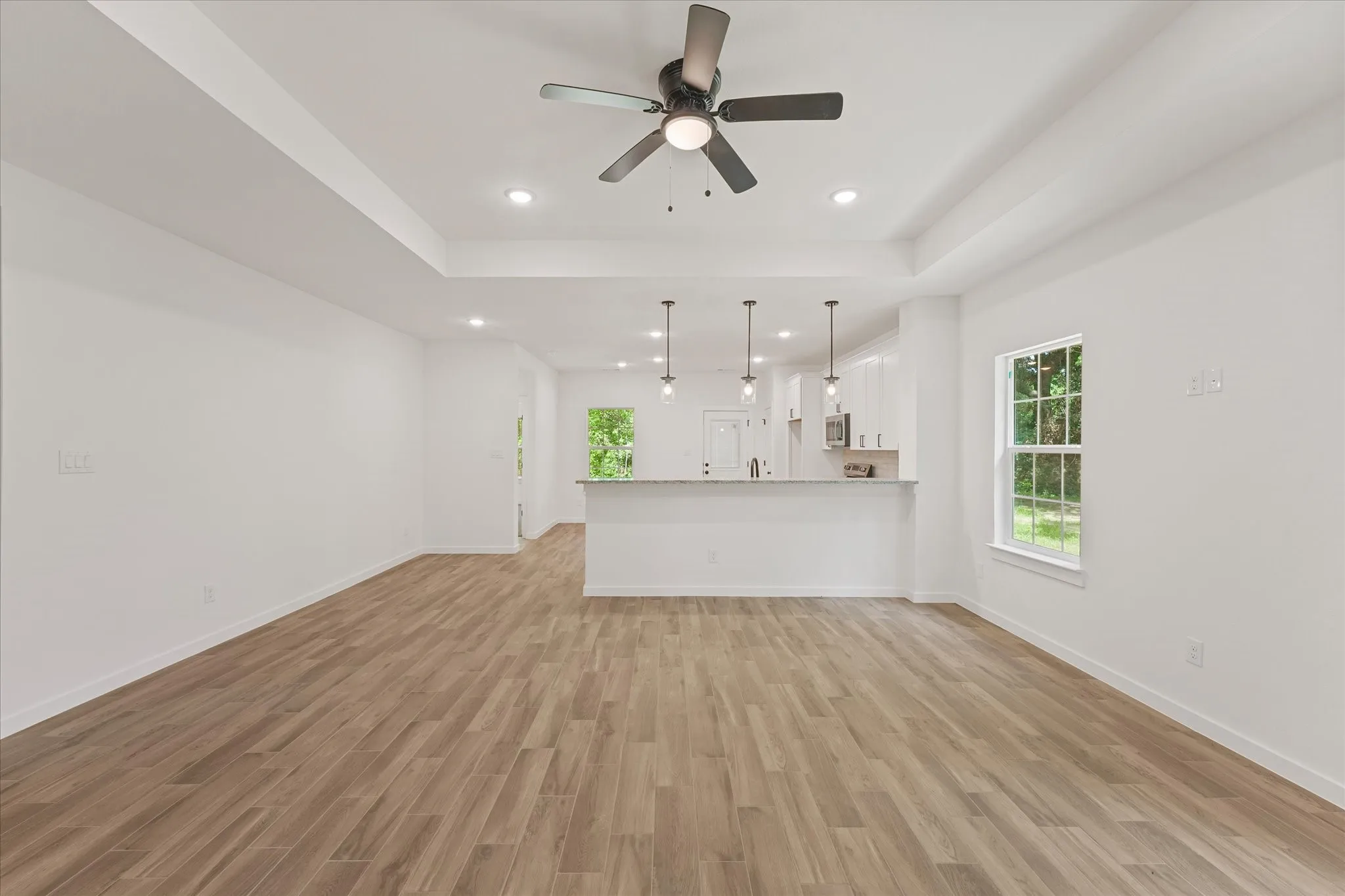 Expansive open-concept living area featuring wood-finish flooring, a tray ceiling, recessed lighting, and a ceiling fan