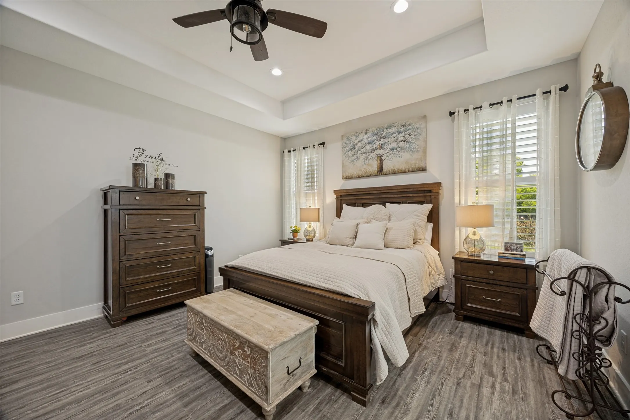 Recessed ceiling with a central fan fixture, wood-finish flooring, and white window shutters