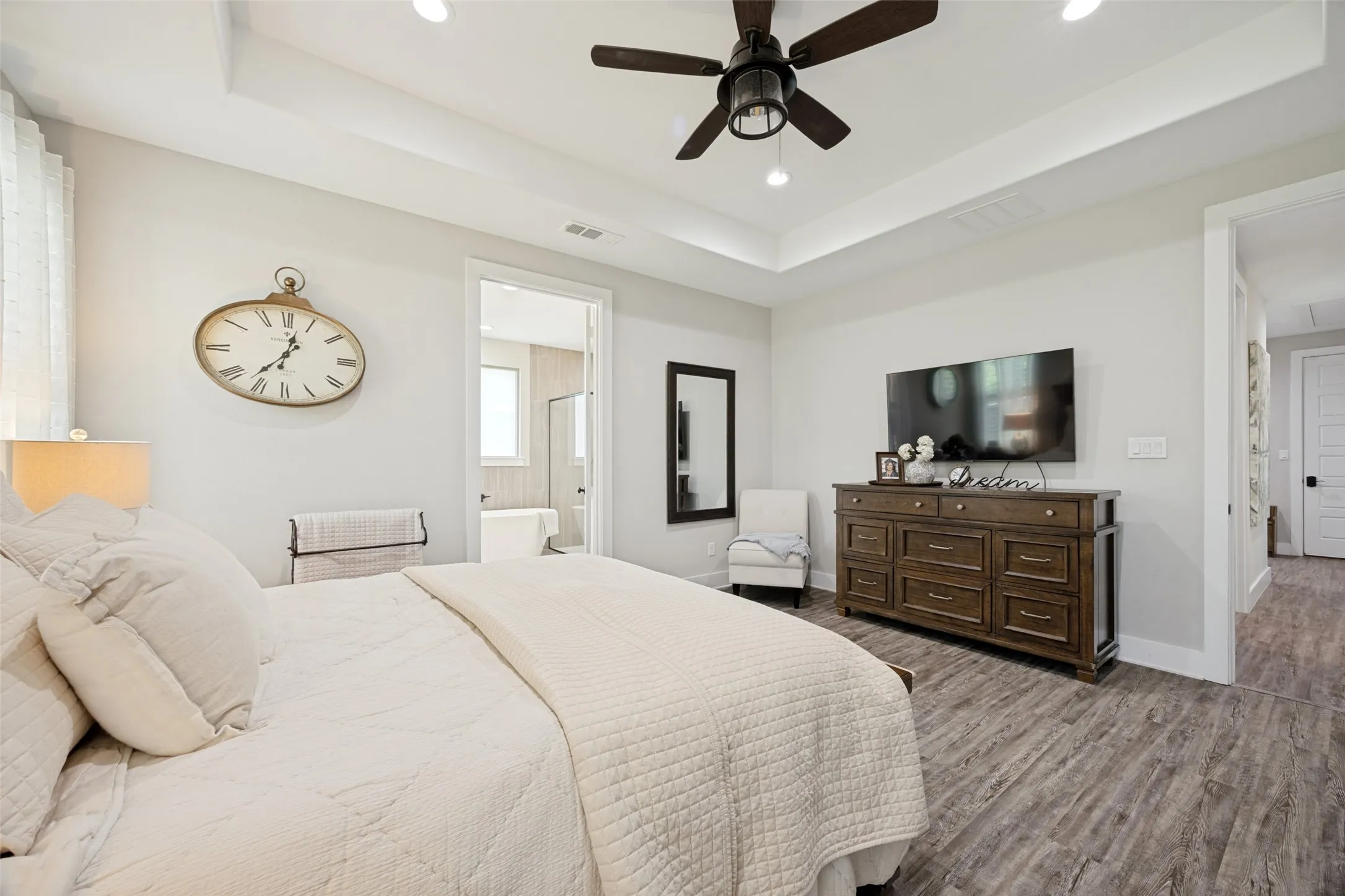Spacious room featuring wood-finish flooring, a tray ceiling, and a ceiling fan with integrated lighting