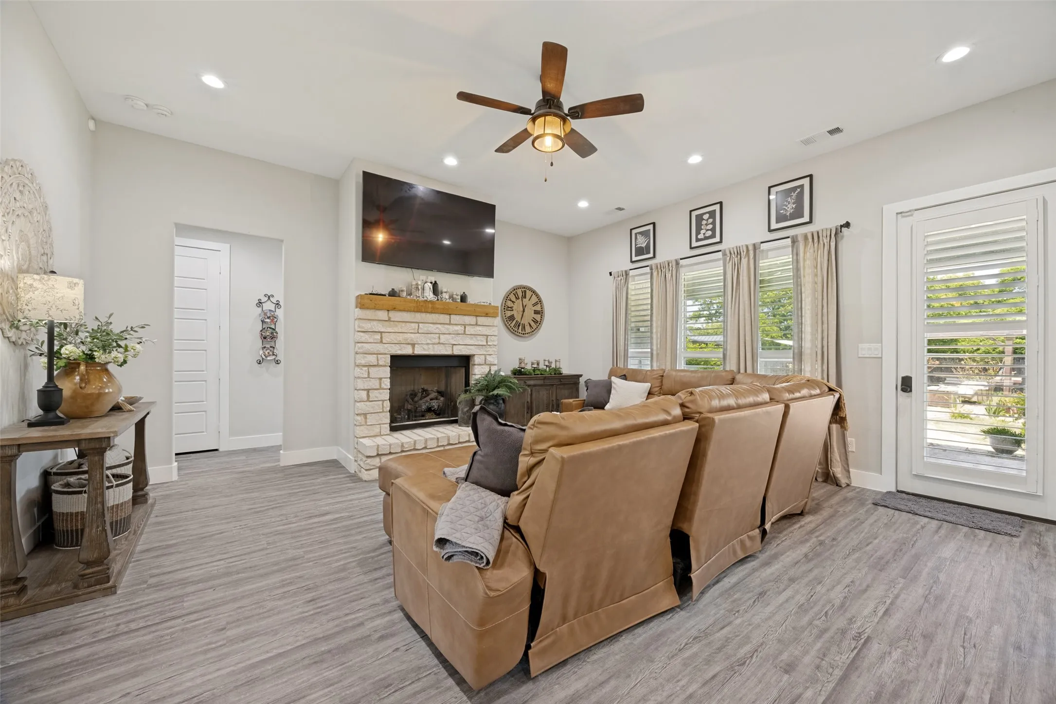 Spacious living area featuring a floor-to-ceiling brick fireplace with a wood mantel, wood-finish flooring, recessed lighting, and a ceiling fan