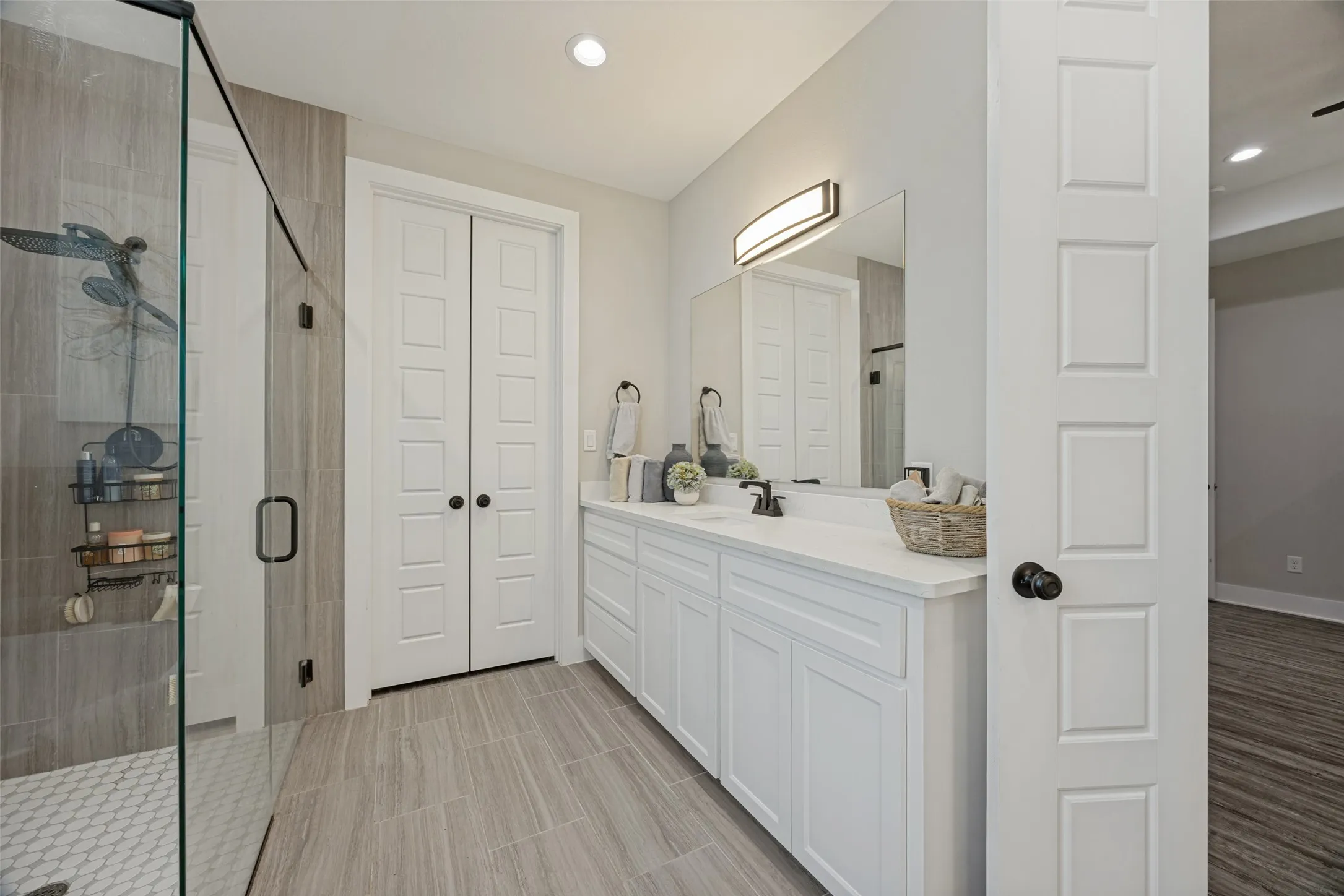 Bathroom featuring a glass-enclosed shower with tile surround, a dual vanity with white cabinetry and granite countertop, and wood-finish tile flooring, large walk in closet