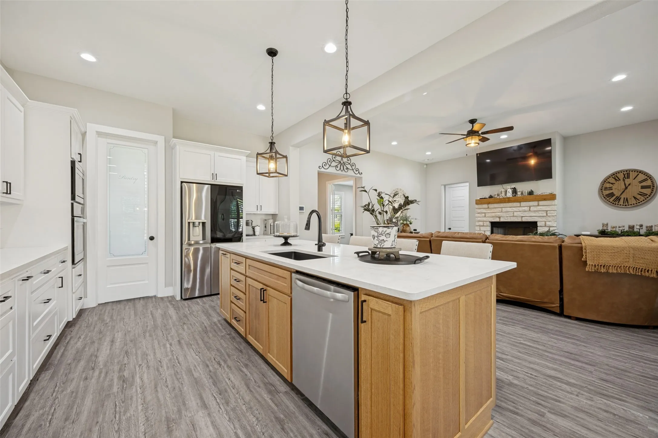 Expansive kitchen featuring a large island with sink, white granite countertops, built-in stainless steel appliances, and wood-finish flooring, decorative lighting and enough space for barstools around the island