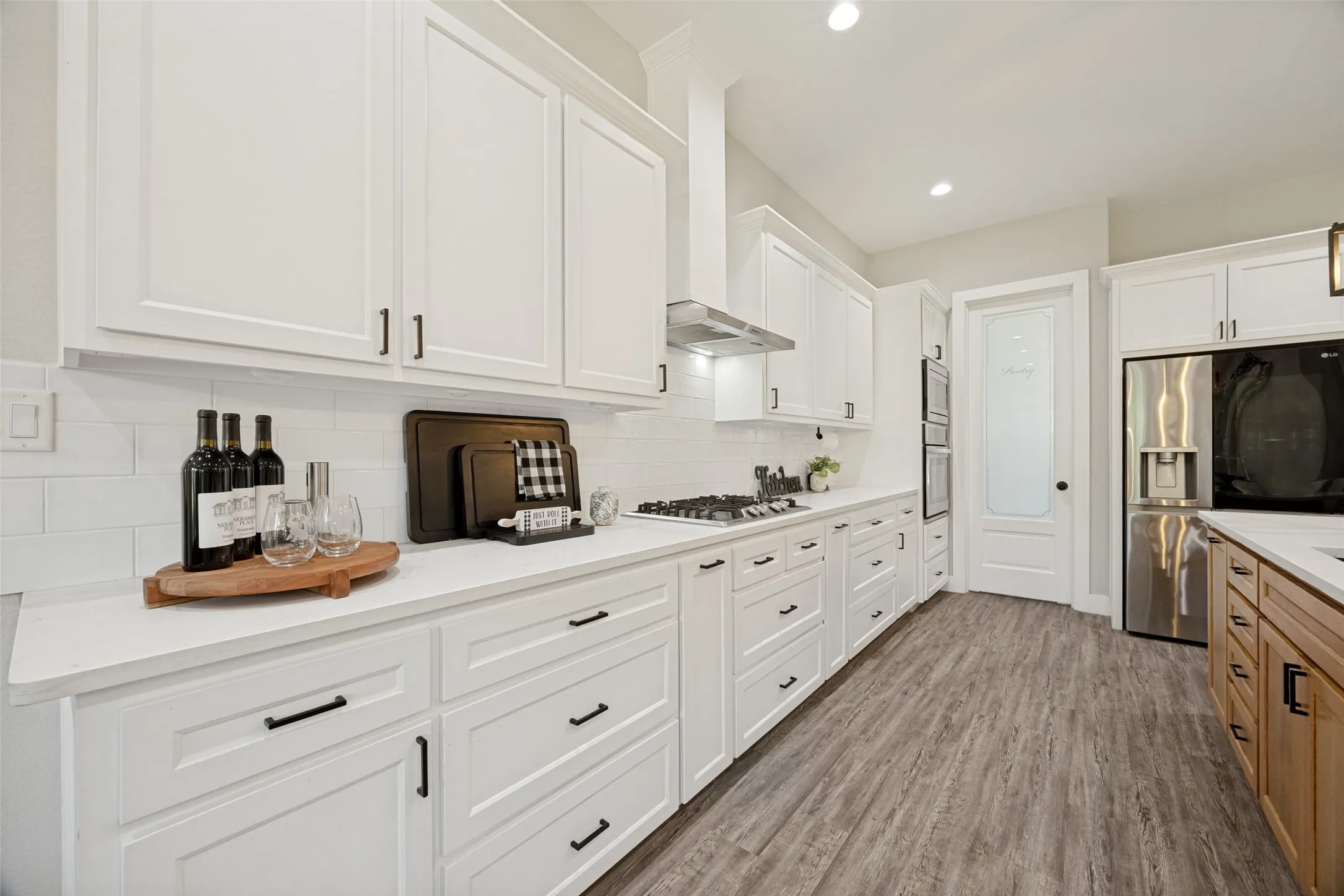 Modern kitchen featuring white cabinetry, light-toned countertops, and wood-finish flooring, large walk in pantry, electric oven,propane gas range top and microwave