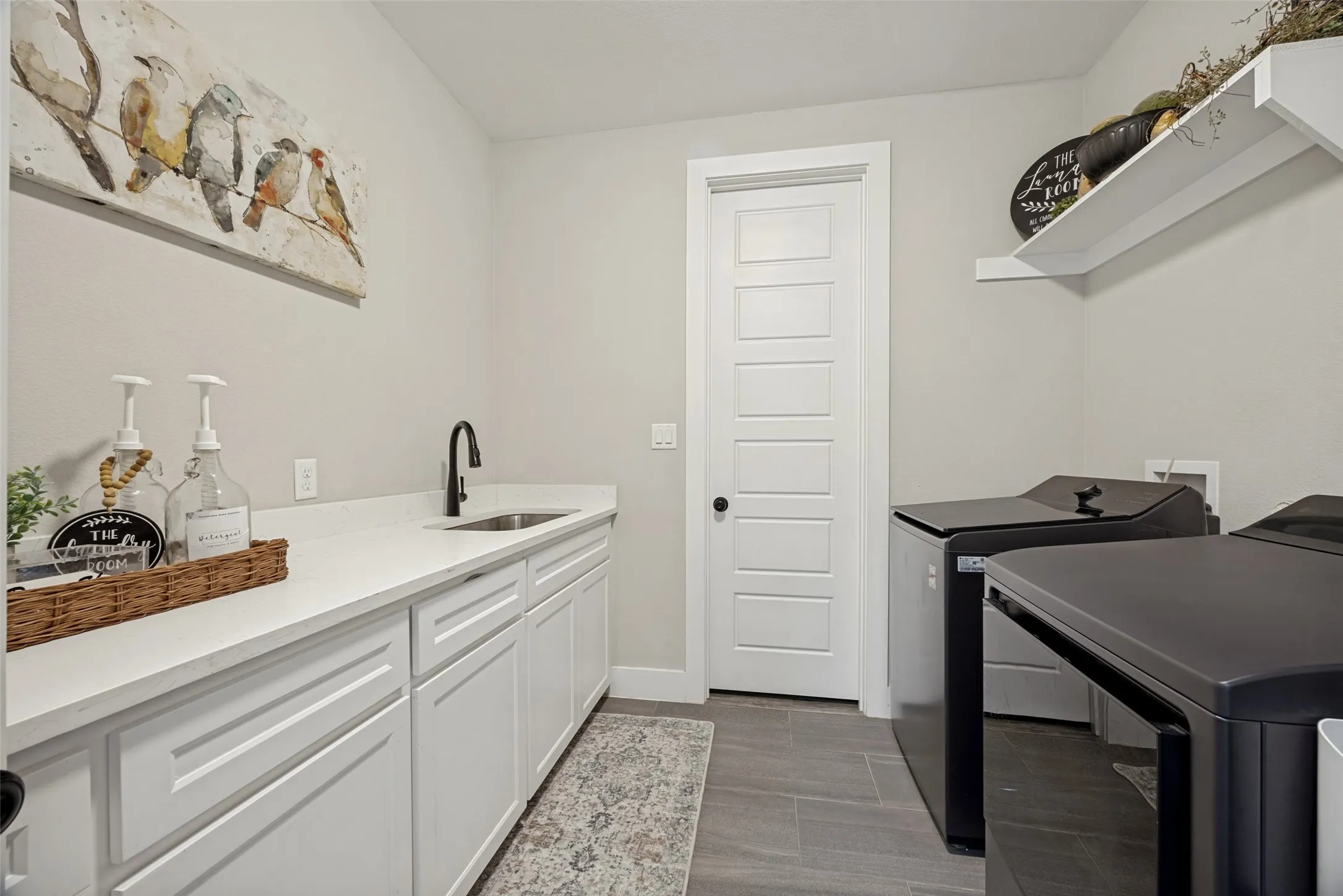 Dedicated laundry space featuring a white paneled door that leads into the primary suite closet, gray tile flooring, and a granite countertop with an undermount sink