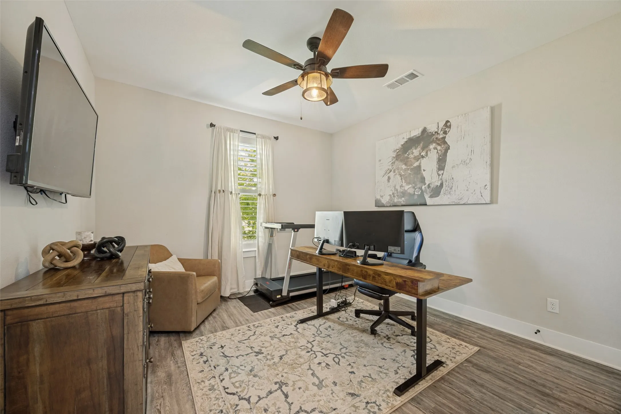 Versatile room featuring wood-finish flooring, a ceiling fan with light fixture, and a window with blinds. This bedroom is being used as a secondary office.