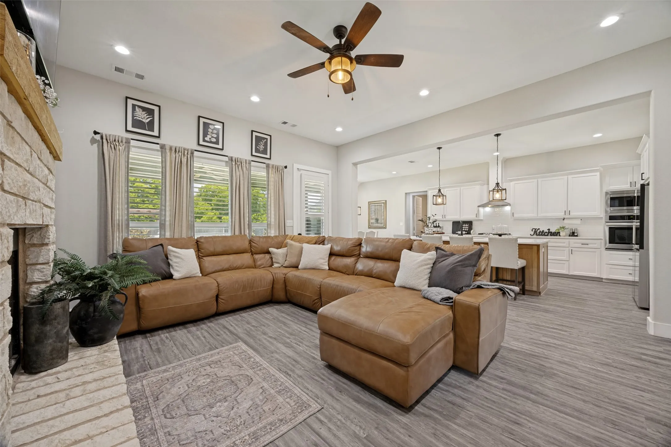 Open-concept living space featuring wood-finish flooring, a stone fireplace, and a ceiling fan