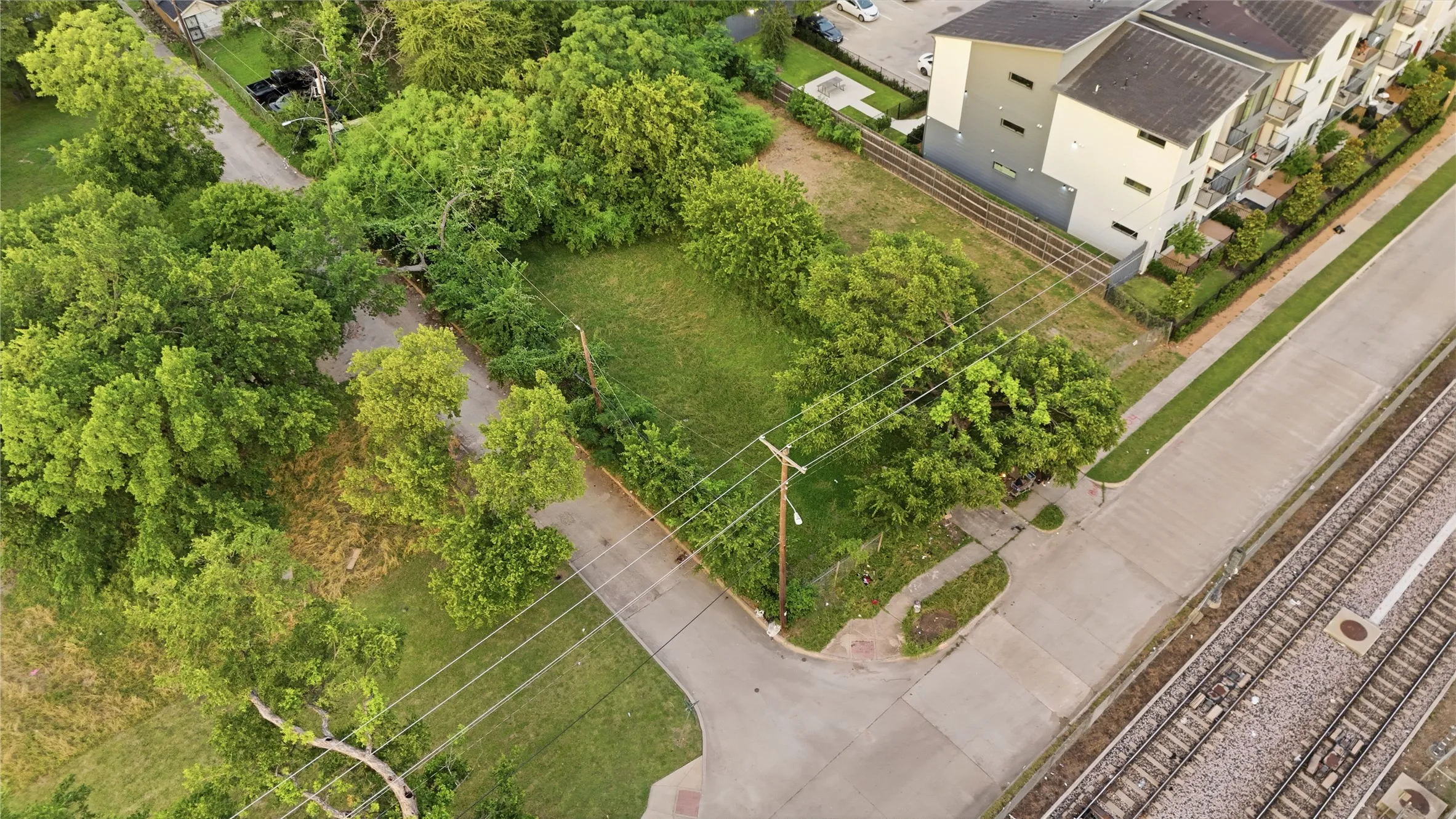 Cleared lot featuring mature trees, surrounding residential structures, and existing paved roads