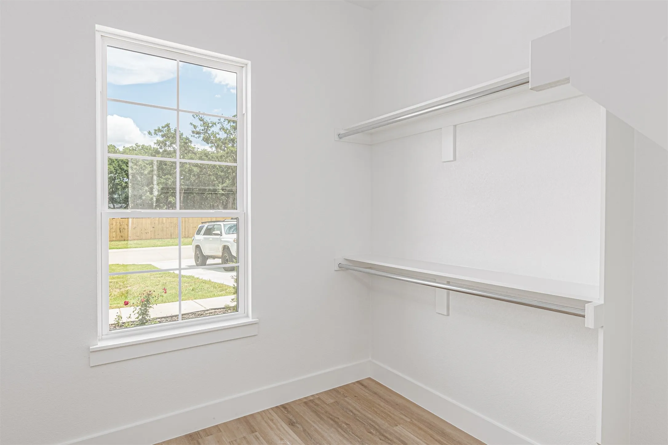 Closet featuring wood-finish flooring, white walls, and a window with grid panes