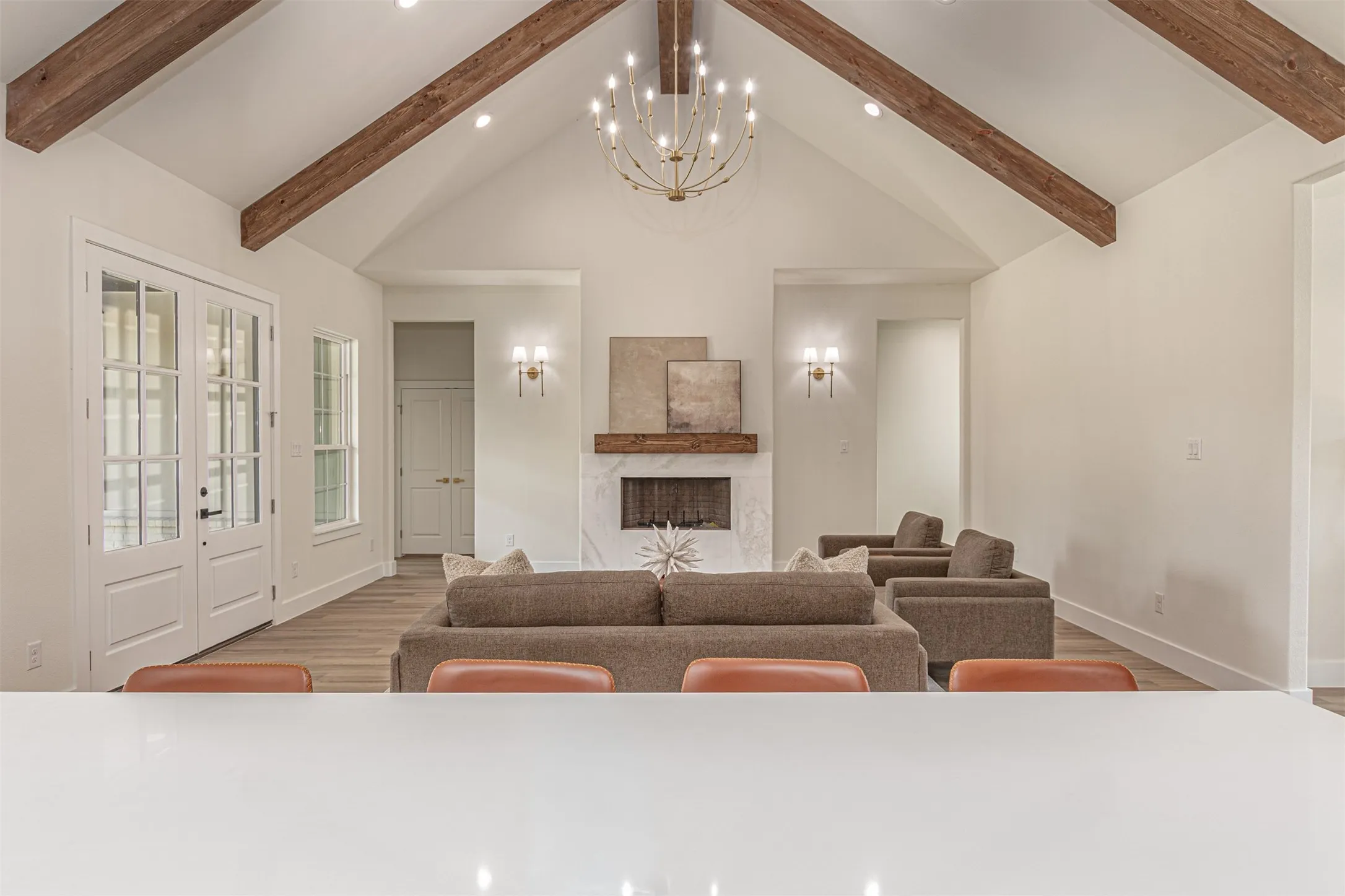 Spacious living area featuring a vaulted ceiling with exposed wood beams, a central chandelier, and recessed lighting